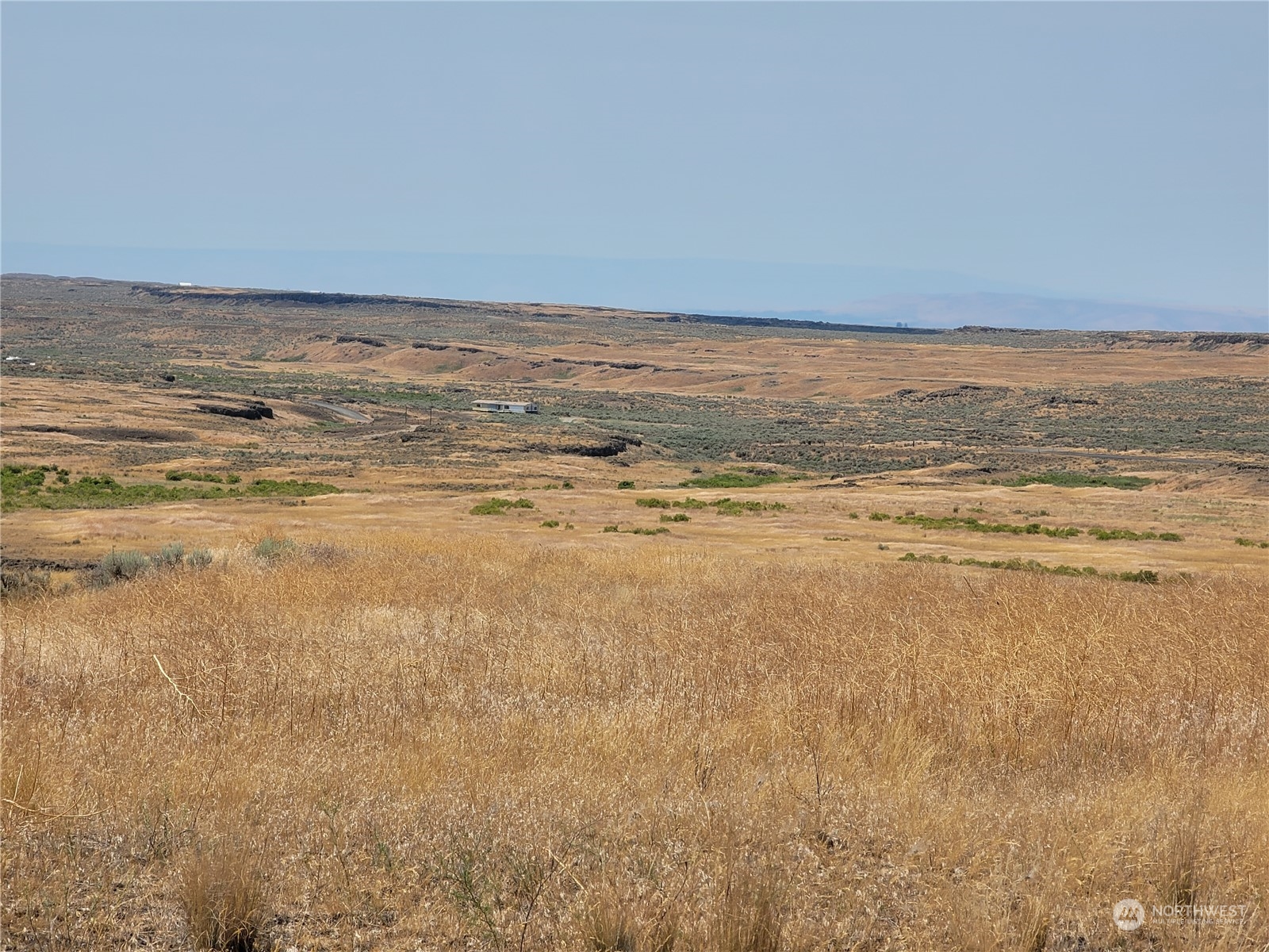 Undeveloped rural lot with golden grass and rolling hills beneath a clear blue sky.