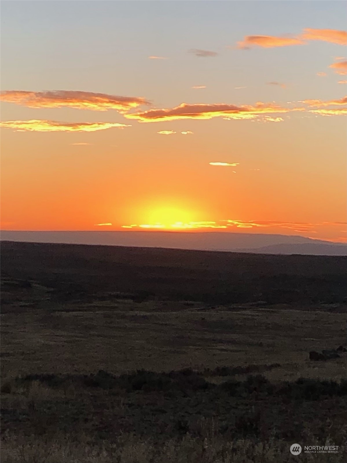 Open land and distant ridgeline silhouetted beneath an orange sunset.