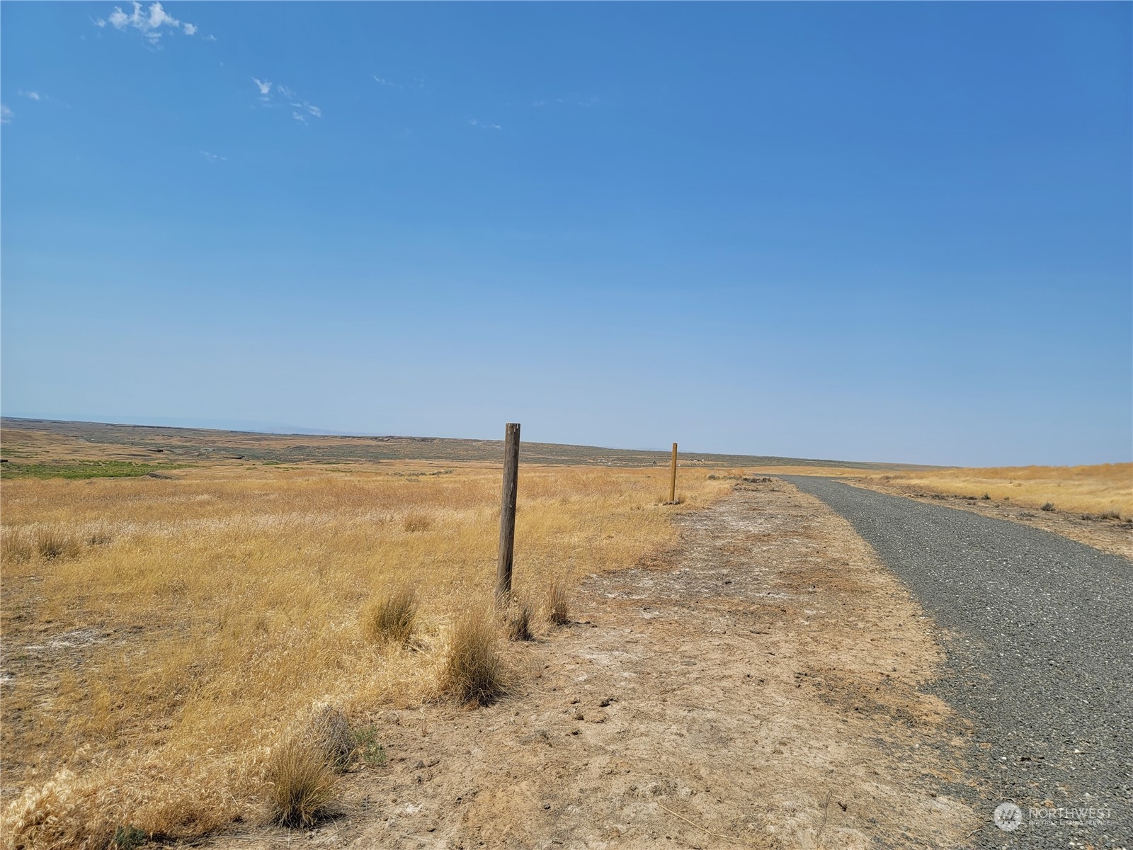 Open dry grassland beside a gravel road, marked by roadside fence posts.
