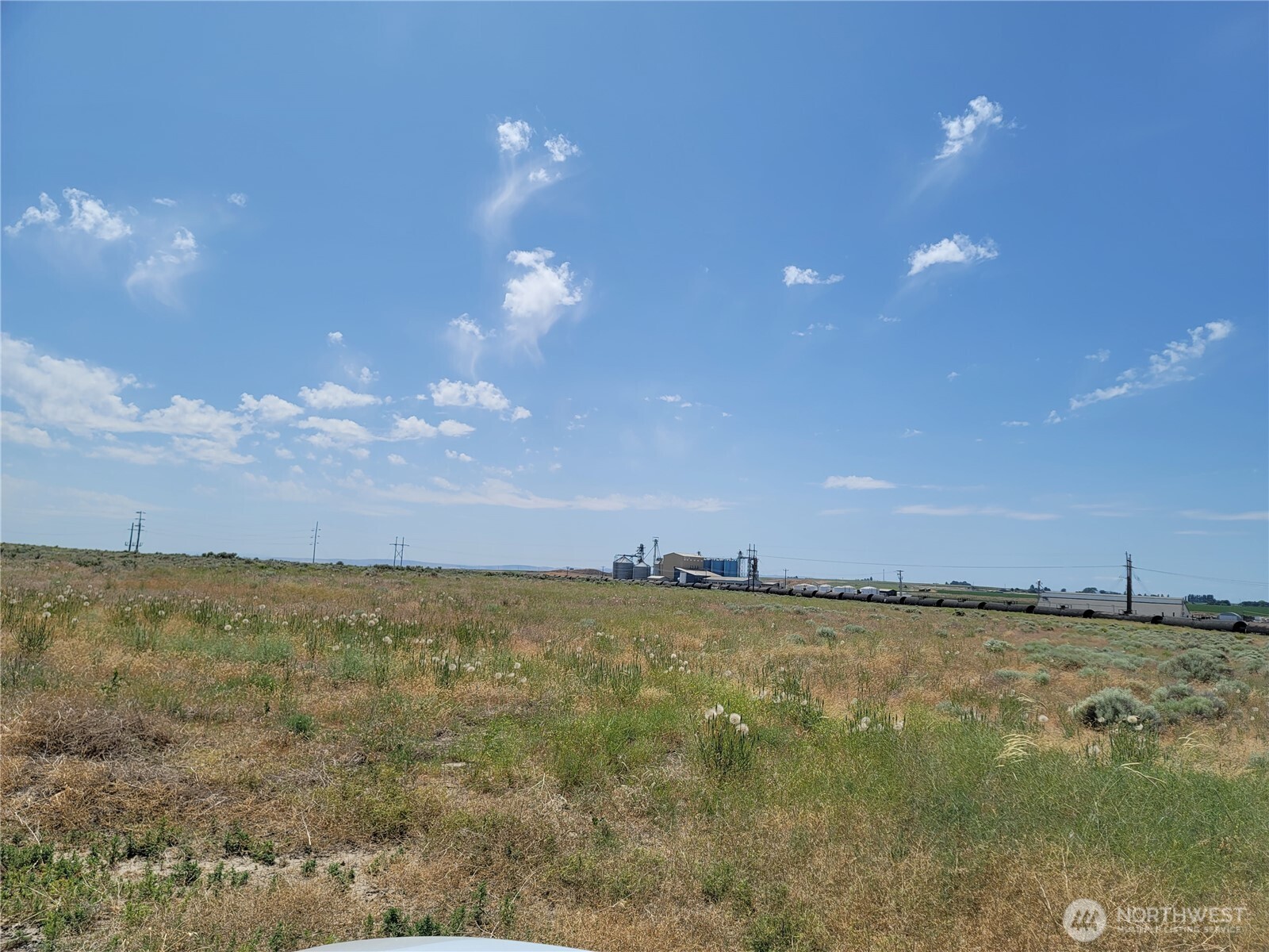 Vacant grassy parcel with railcars and grain-handling structures along the distant horizon.