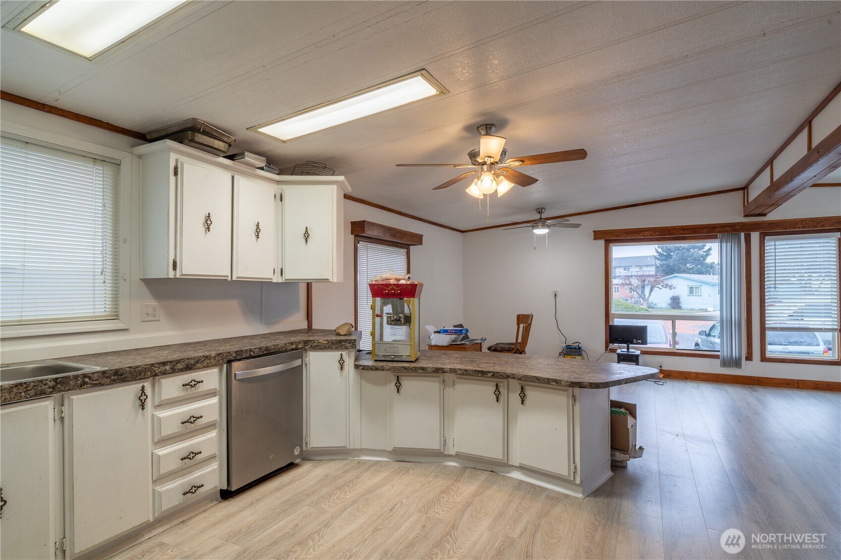 Kitchen with white cabinets and a long peninsula opening into a living area.