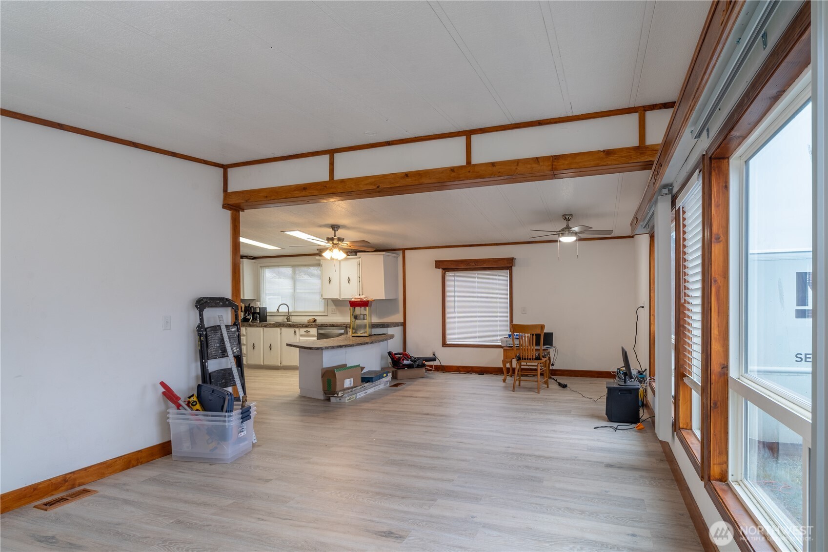 Open living area with a kitchen, light flooring, wood trim, and tall windows.