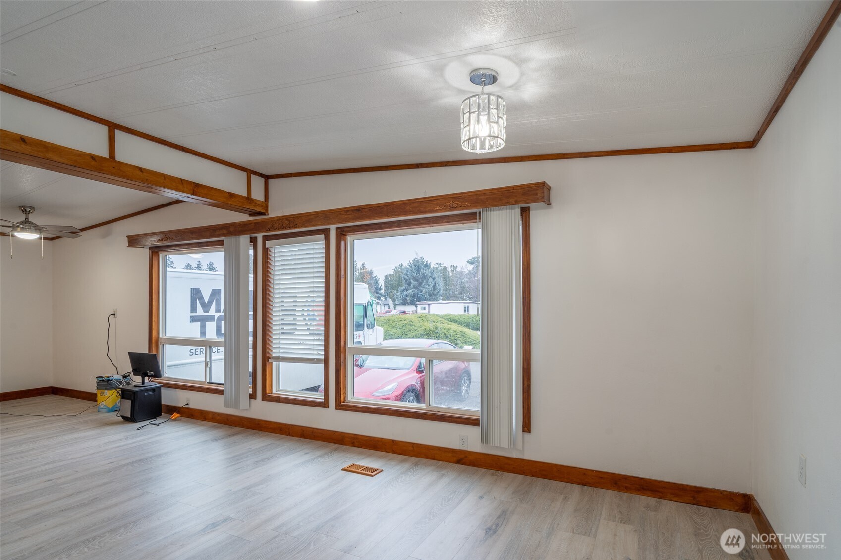 Vacant interior room with large wood-trimmed windows, decorative beams, and light flooring.
