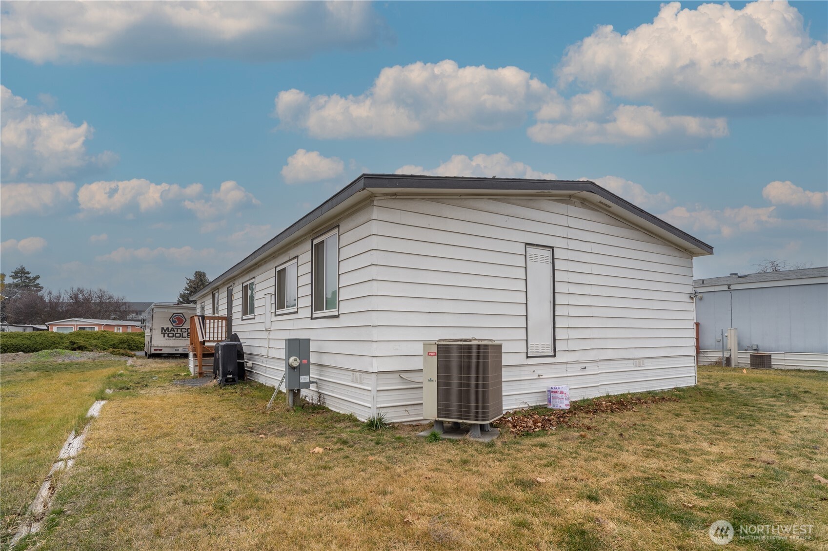 White manufactured home with horizontal siding and an outdoor HVAC unit beside dry grass.