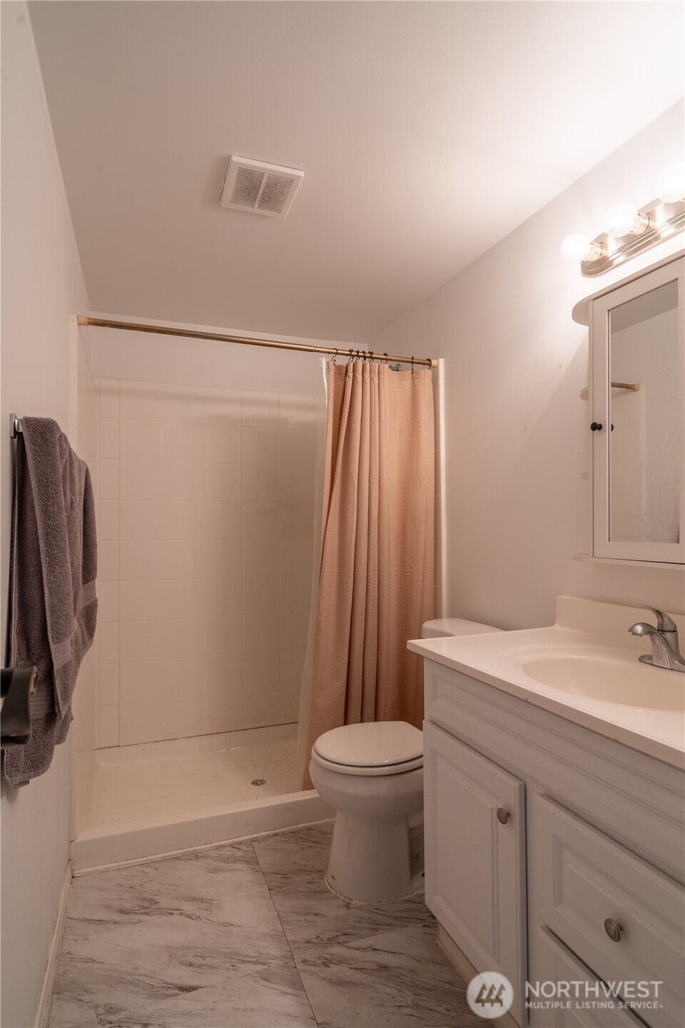 Bathroom with a tiled shower, peach curtain, white vanity, and marble-patterned floor.