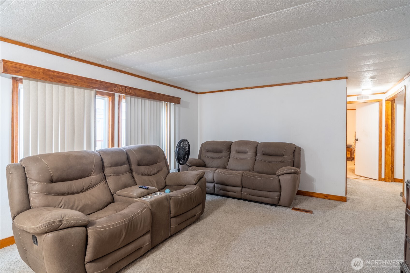 Living room with two brown reclining sofas, beige carpet, and wood-trimmed windows.