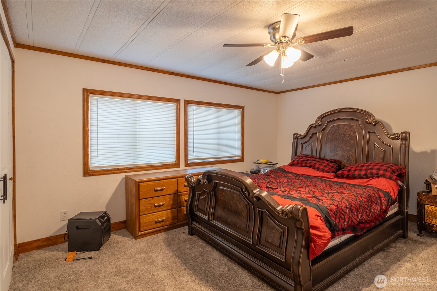 Bedroom with an ornate dark wood bed, red and black bedding, and two windows with blinds.