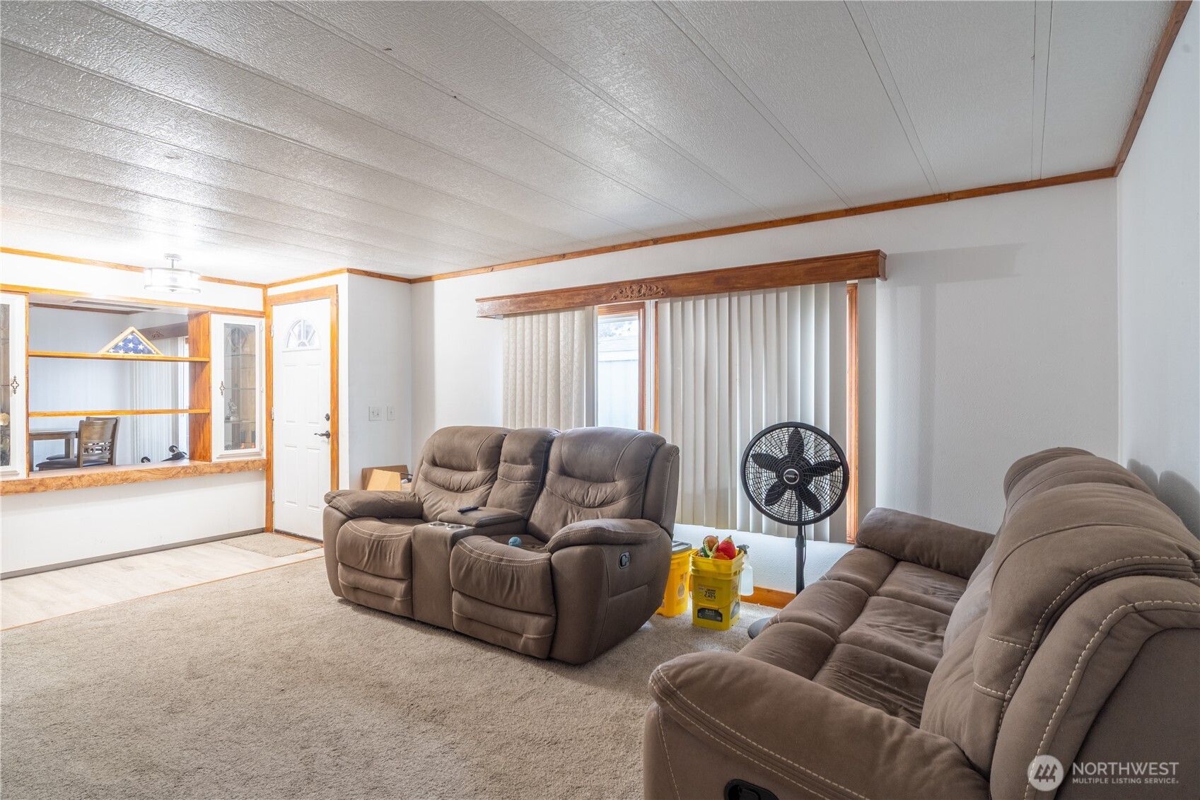 Living room with brown reclining sofas, beige carpet, and a wood-trimmed pass-through.