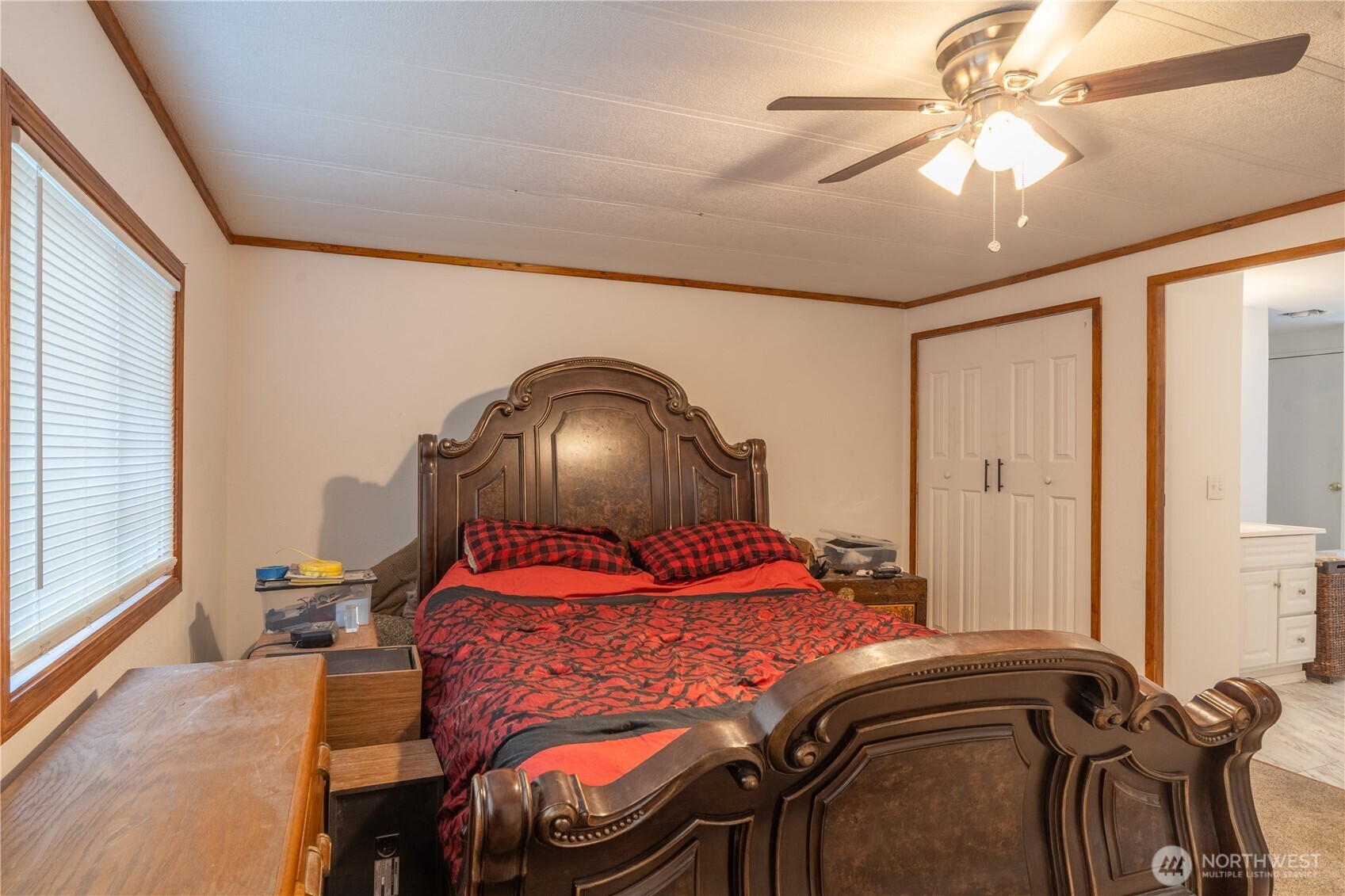 Furnished bedroom with an ornate dark wood bed, red-and-black bedding, and a window with white blinds.