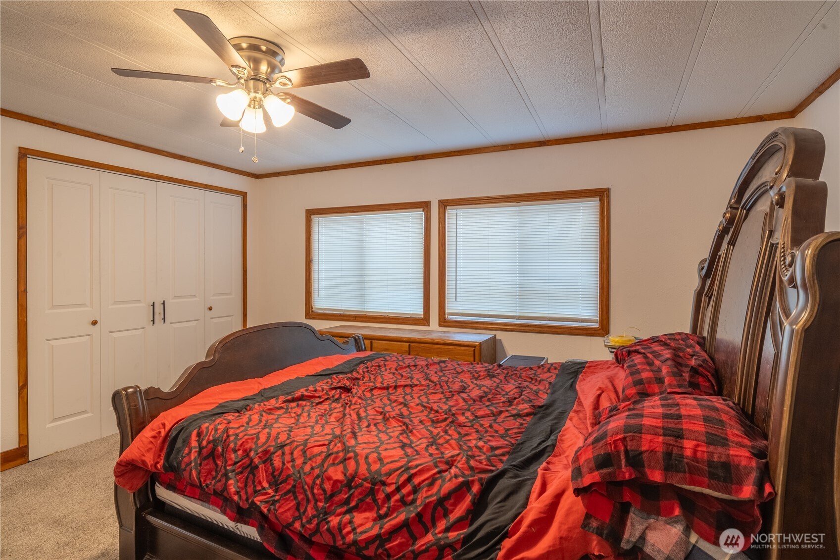 Bedroom with a dark wood bed, red and black bedding, white closet doors, and two windows.