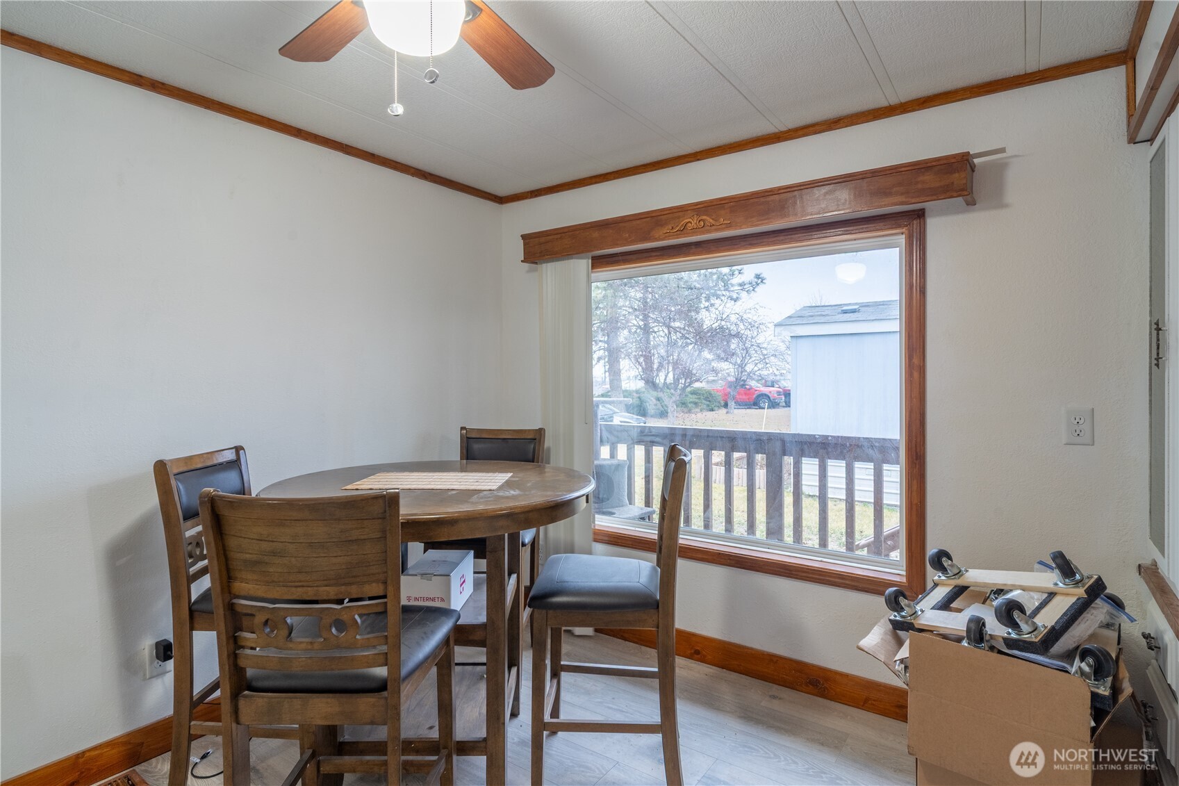 Dining area with a round wooden table, chairs, and a large window overlooking a deck.