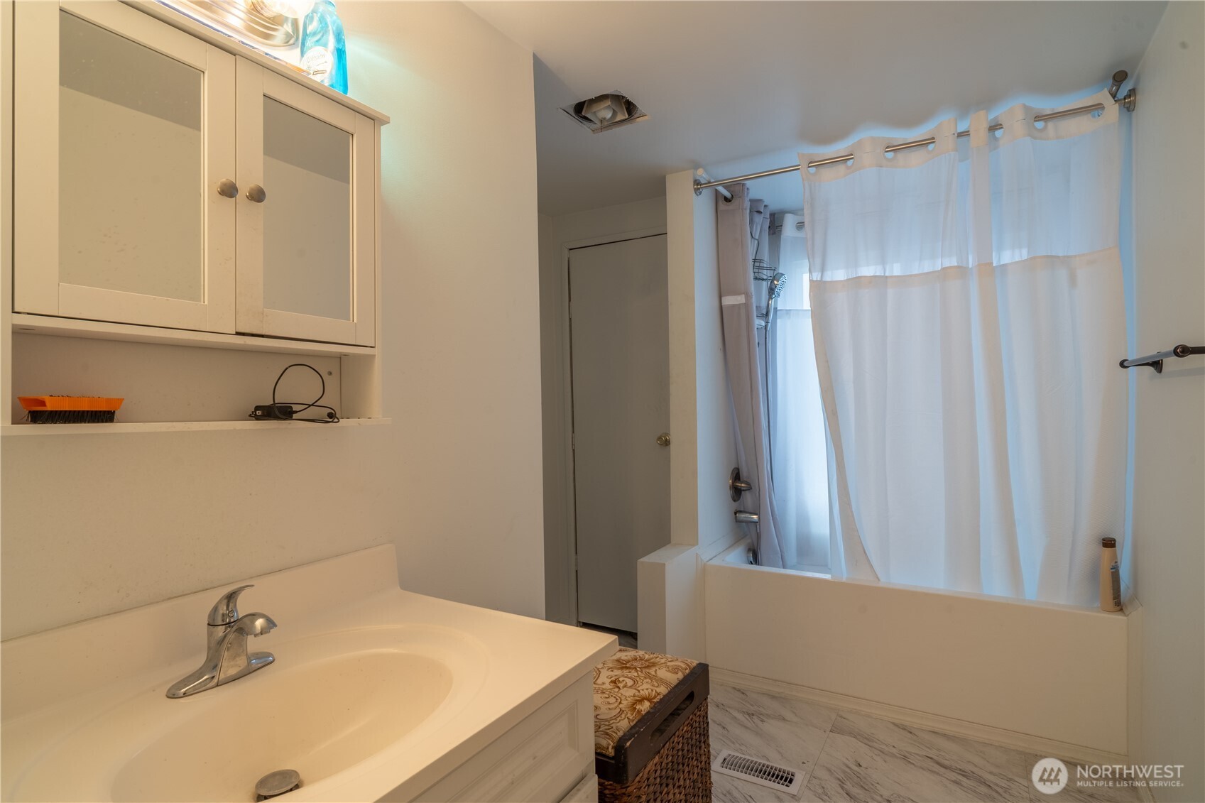 Bathroom with a white vanity, wall cabinet, curtained bathtub, and marble-look tile floor.