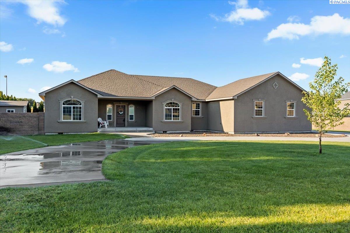 Gray single-story home with arched windows, a covered entry, and a broad green lawn.