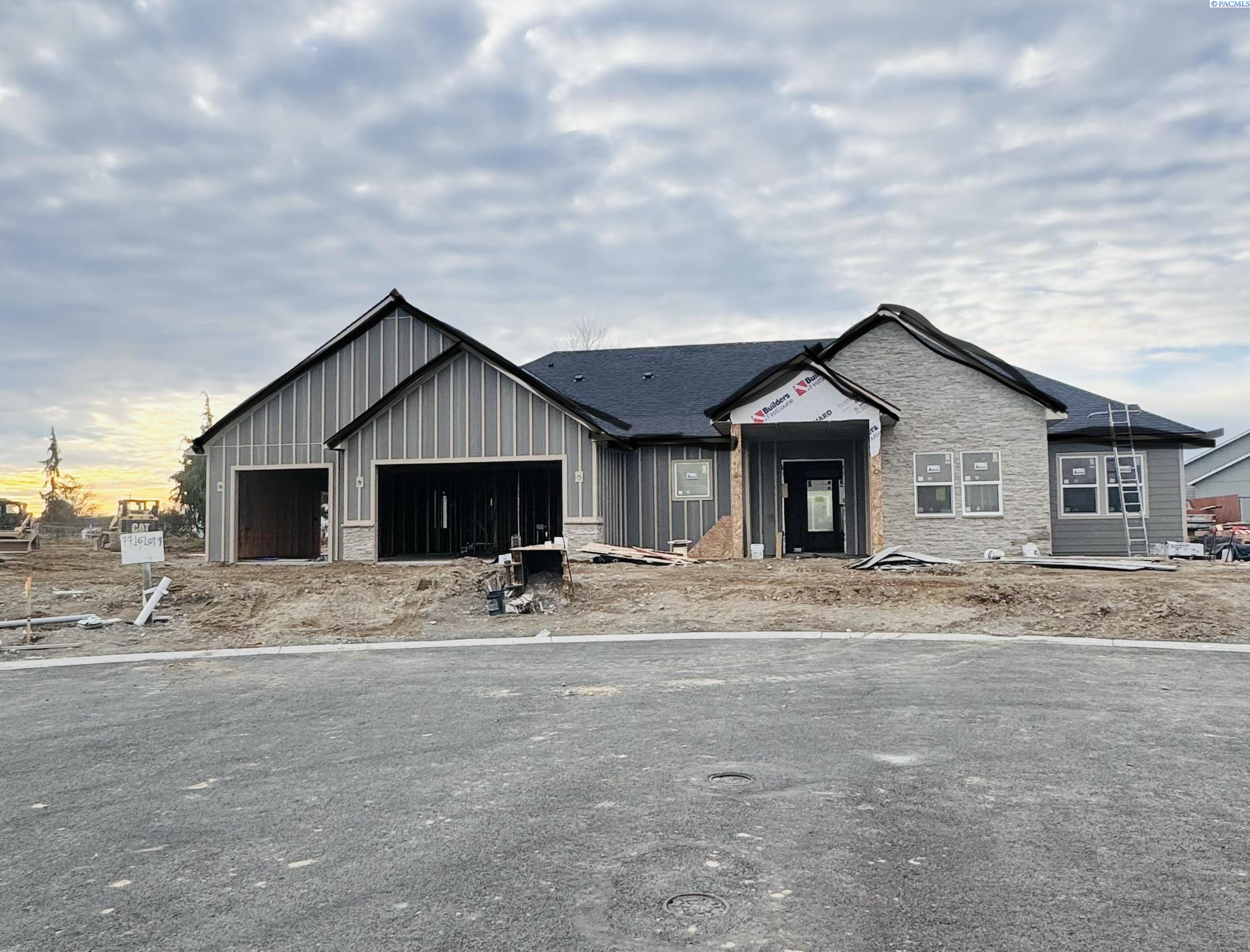Large gray house under construction with stone accents, open garage bays, and a ladder at the side.