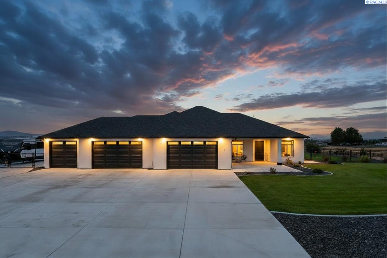 Single-story home with three black garage doors and a broad driveway at dusk.