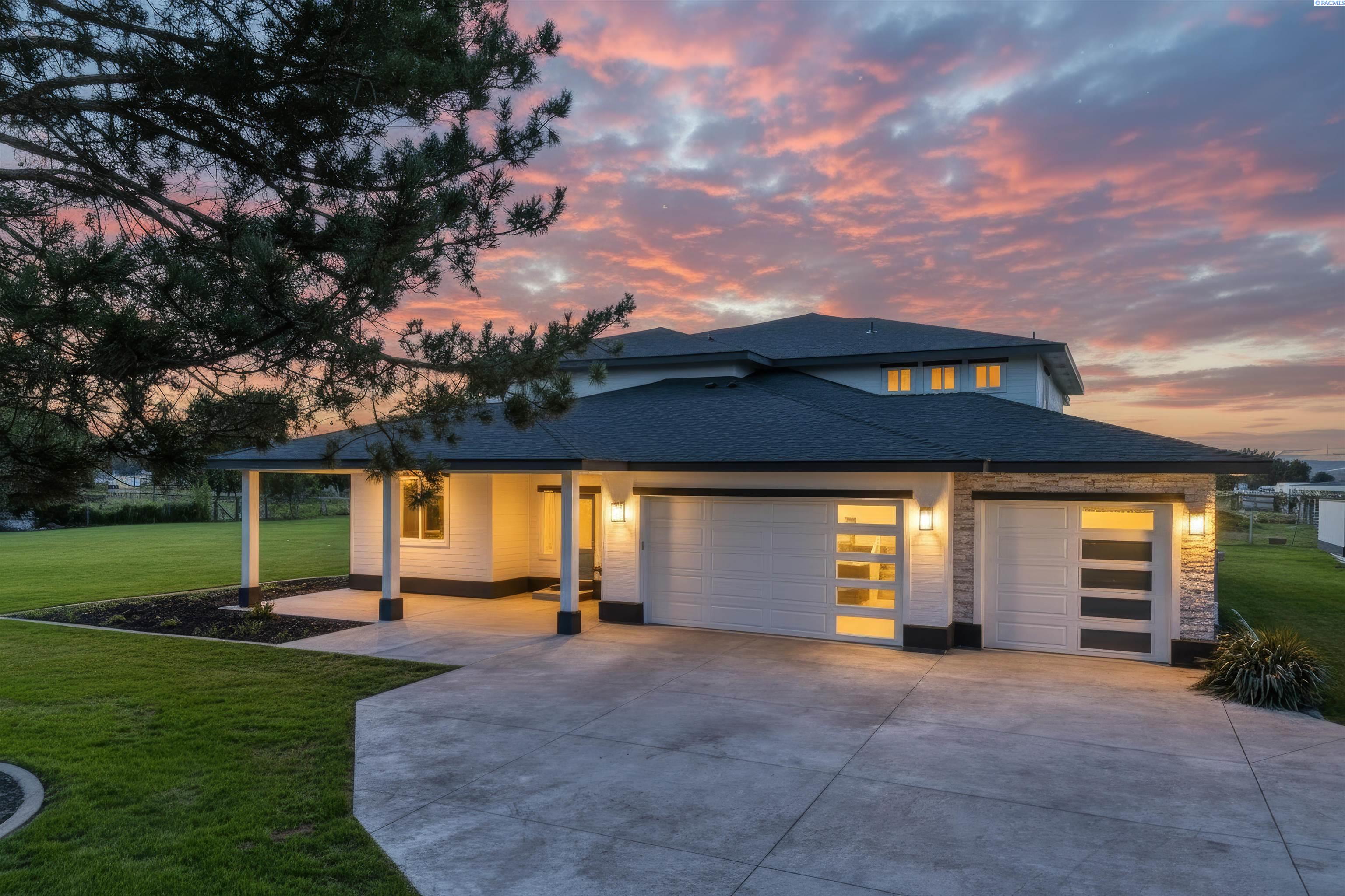 Modern house with two garage doors and a wide driveway beneath a pink sunset sky.