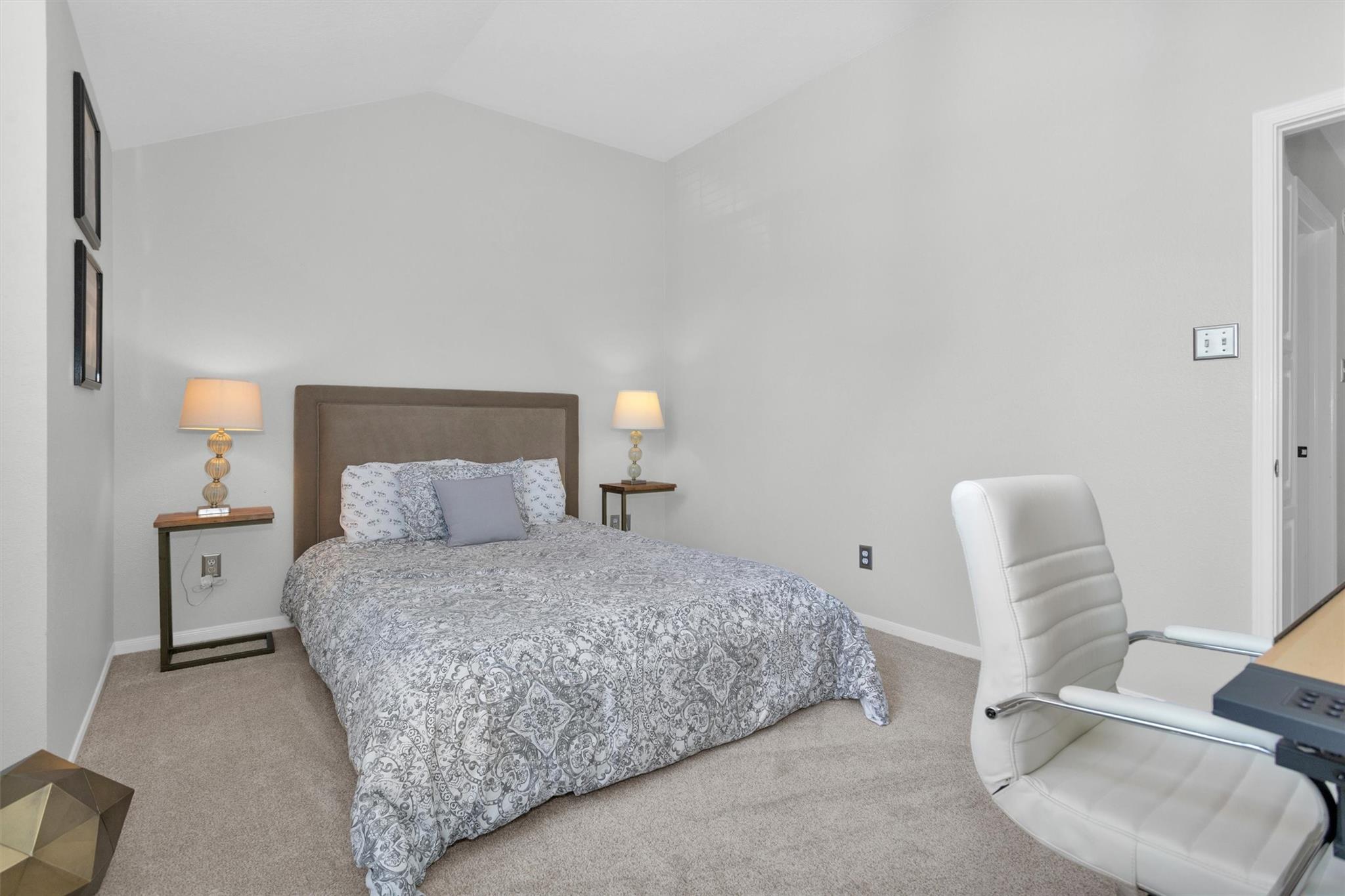 Furnished bedroom with a patterned bed, matching bedside lamps, and a white office chair.