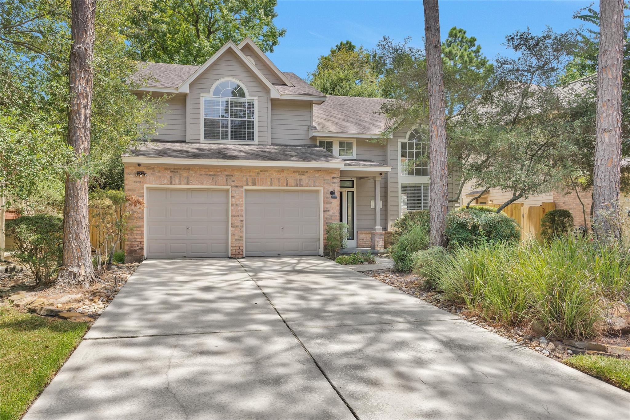 Two-story gray-and-brick house with a double garage, broad driveway, and mature trees.