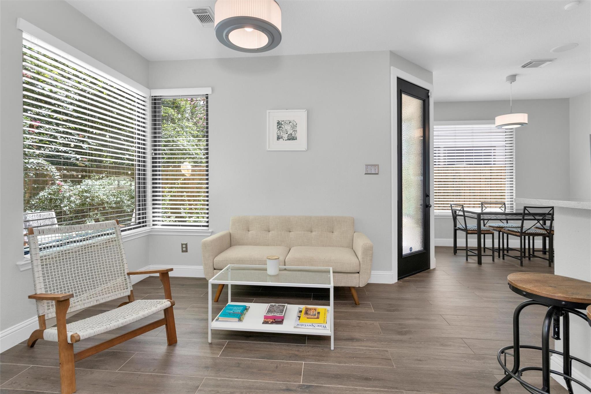 Staged living room with beige sofa and corner windows, opening into a dining area.