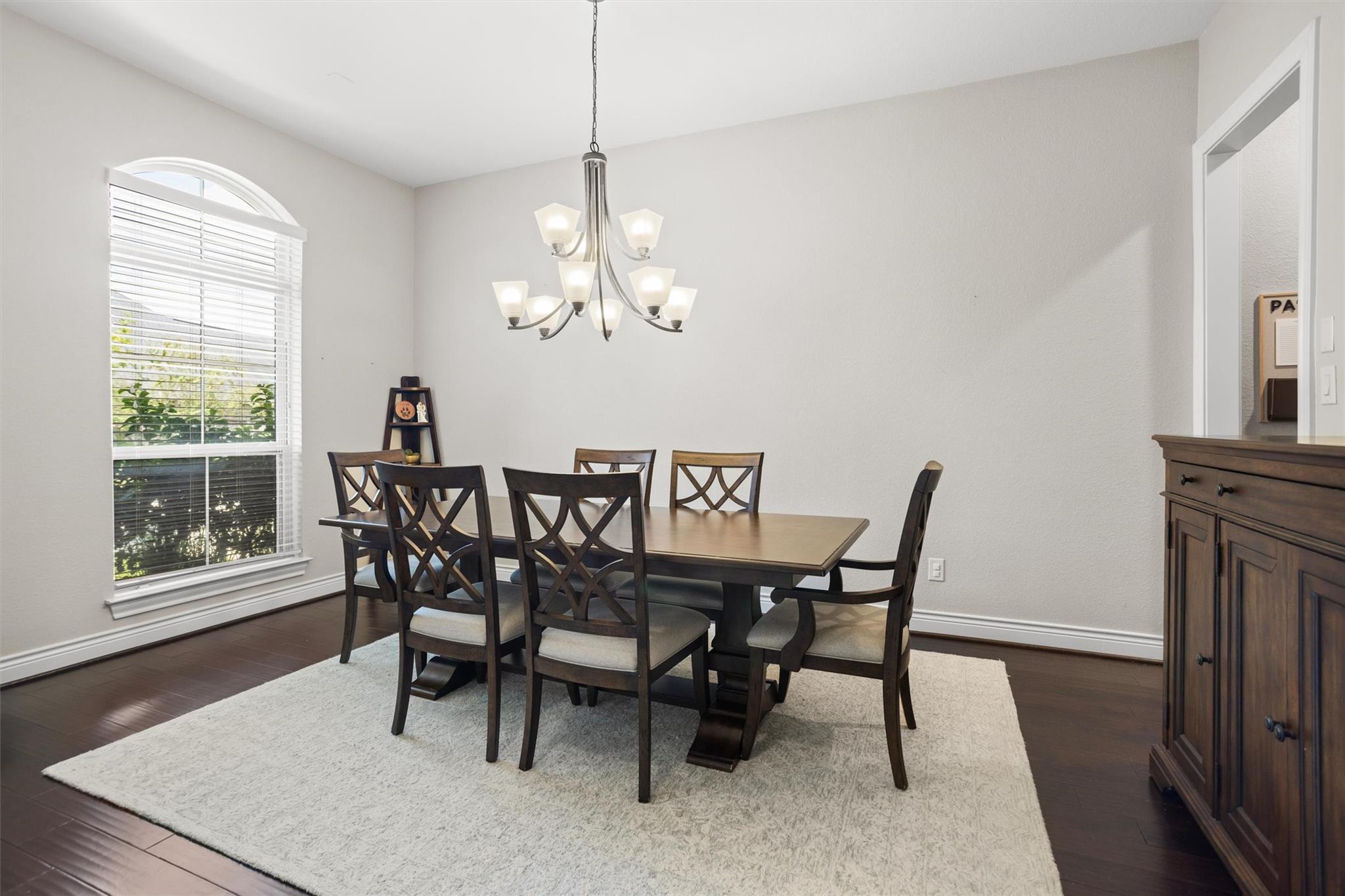 Furnished dining room with a dark wood table, cross-back chairs, and a large arched window.