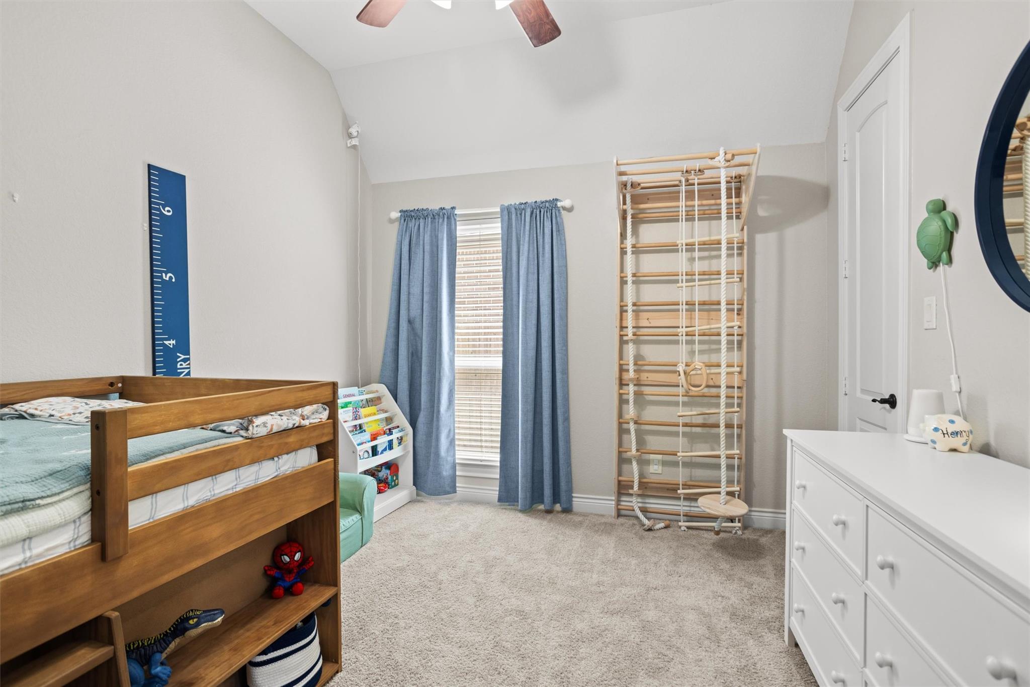 Child’s bedroom with a wooden bed, wall climbing gym, blue curtains, and white dresser.