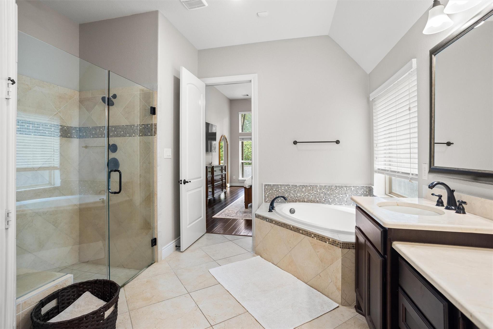 Primary bathroom with a glass shower, built-in soaking tub, and dark wood double vanity.