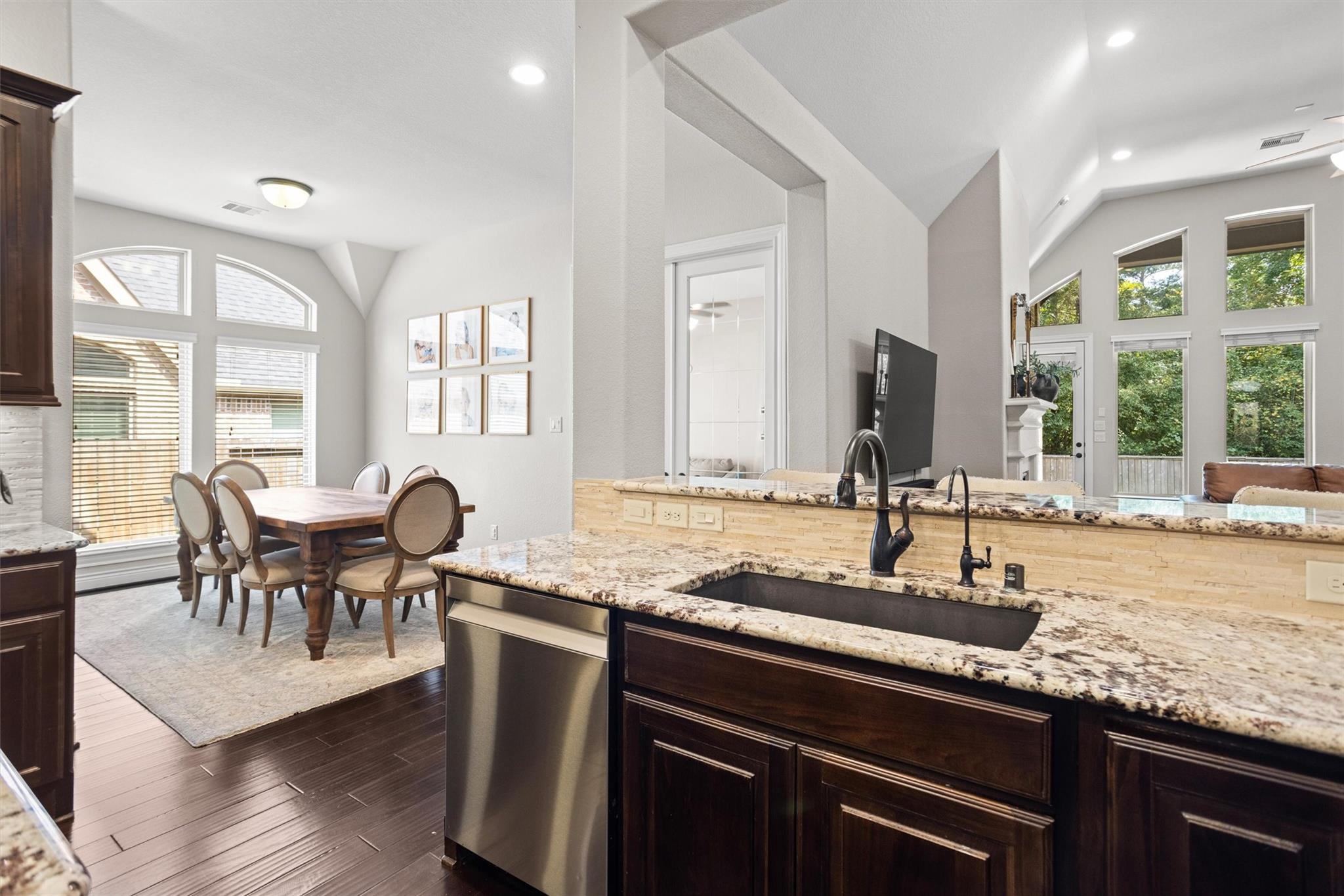 Open kitchen with granite island and dark wood cabinets beside a dining area with arched windows.
