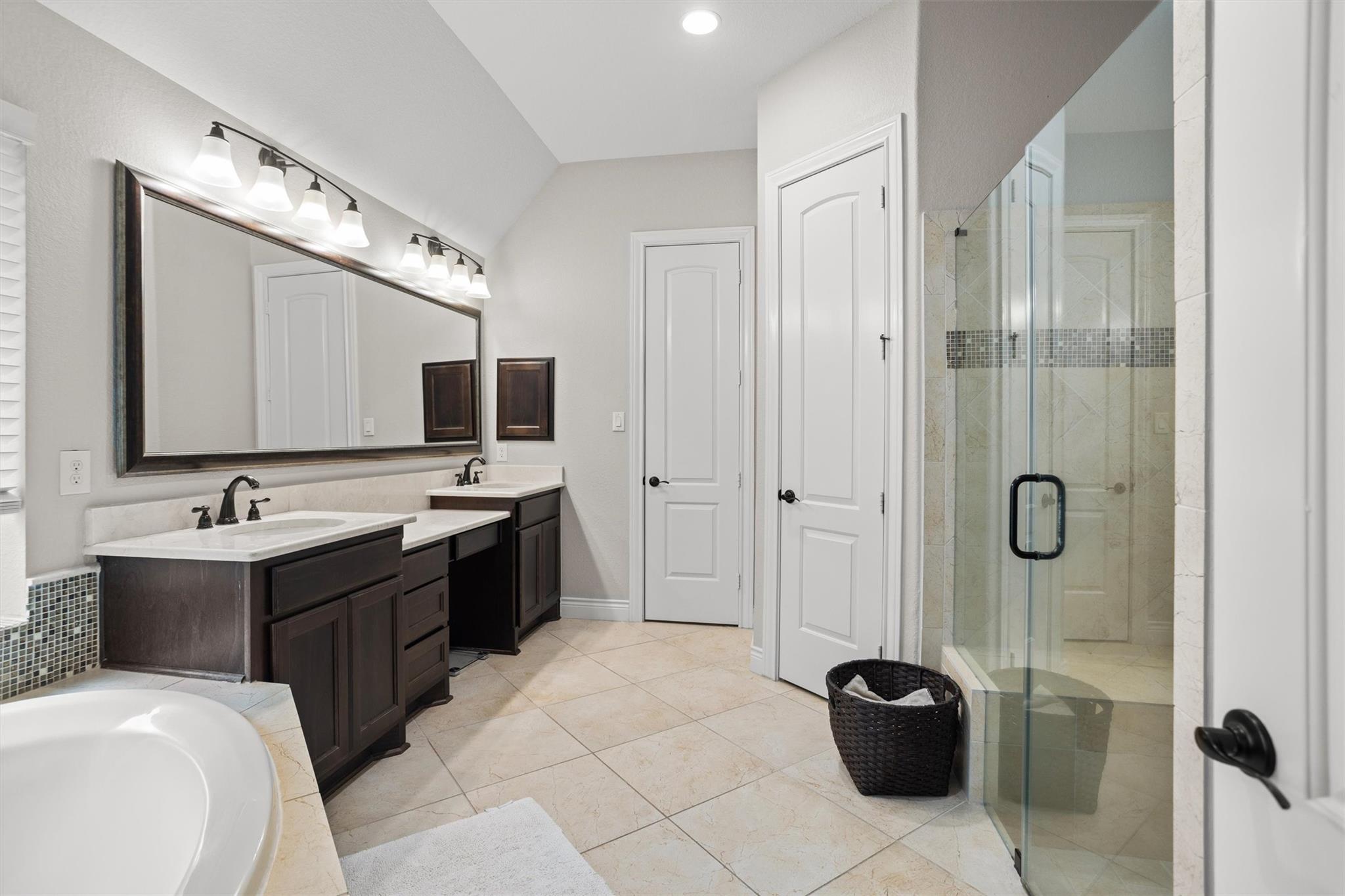 Primary bathroom with a dark double vanity, glass shower, and soaking tub.