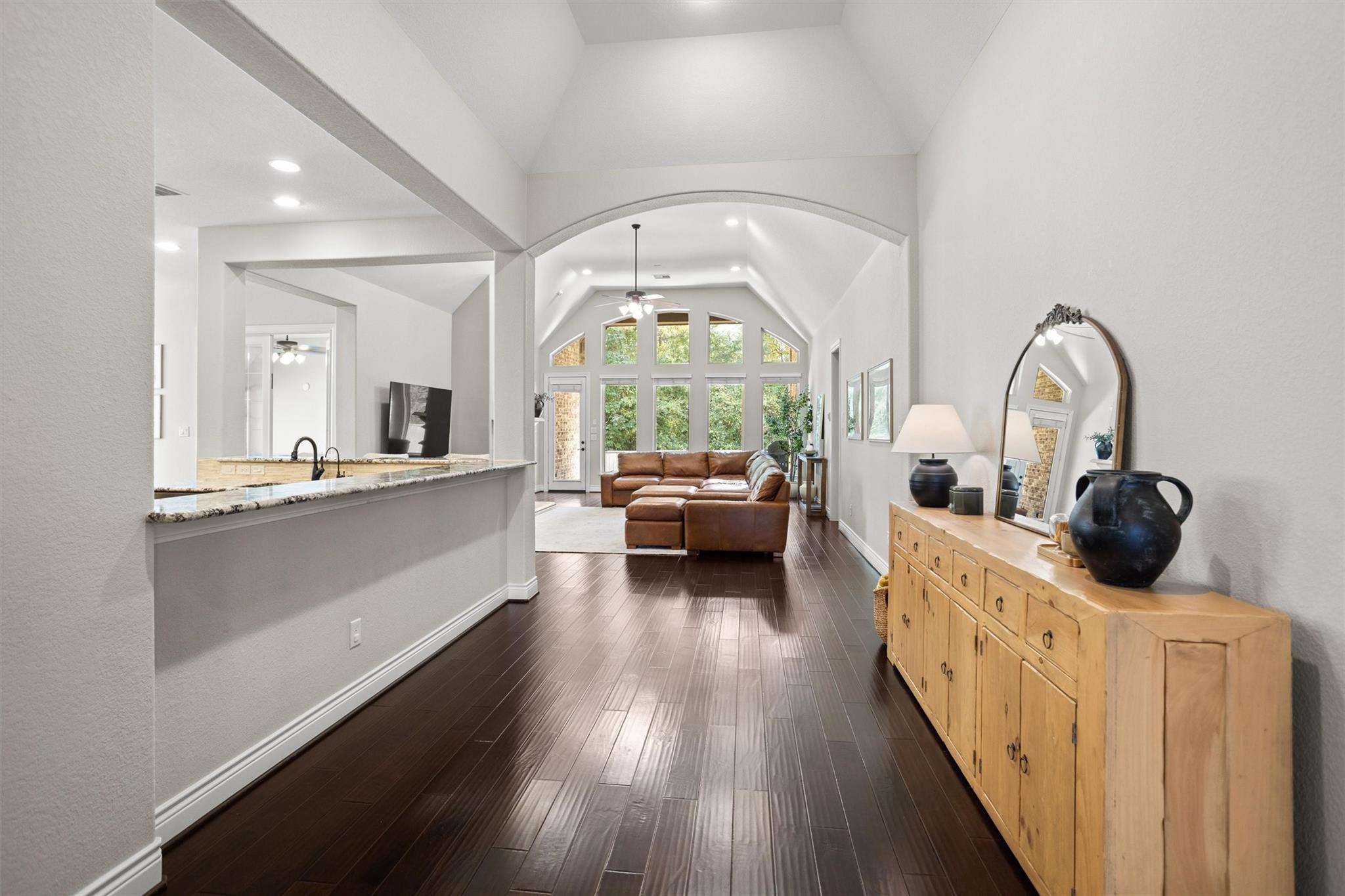 Open-plan living room with vaulted ceiling, tall windows, brown sectional, and dark wood floors.