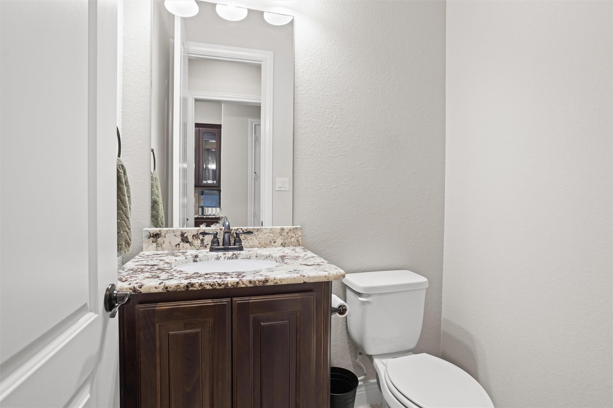 Bathroom with dark wood vanity, mottled stone countertop, large mirror, and white toilet.