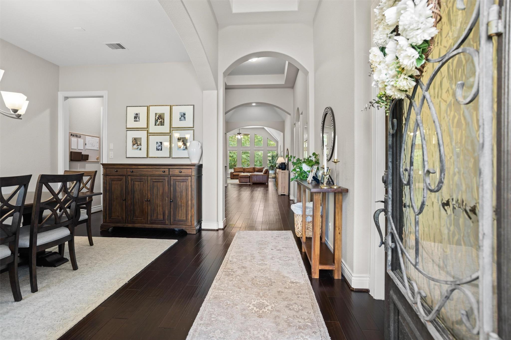 Furnished entry hall with arched openings, dark hardwood floors, and an ornate glass front door.