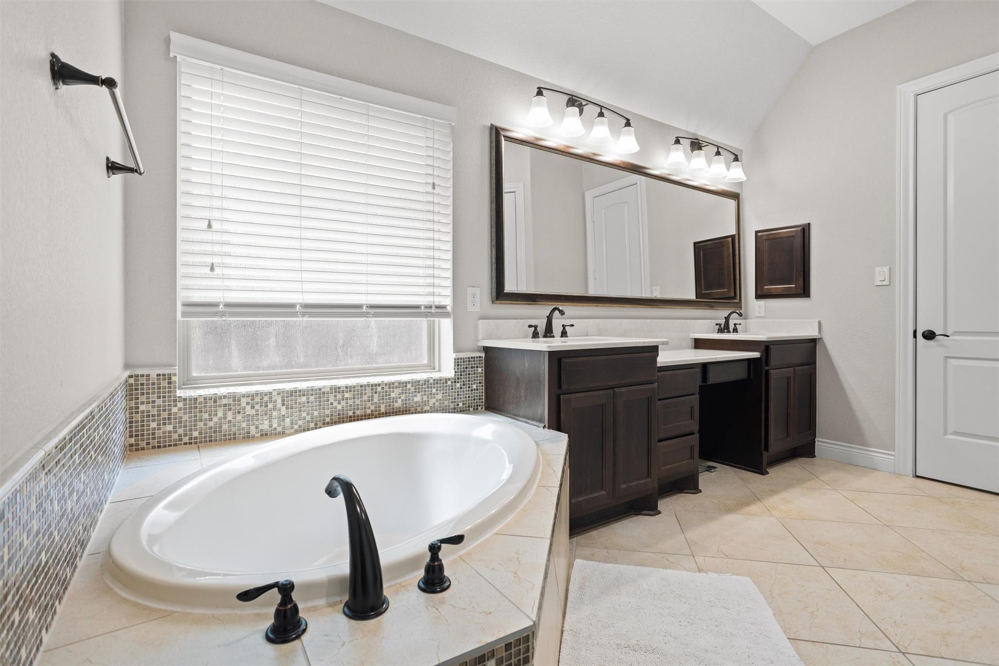 Bathroom with an oval soaking tub and two dark-wood vanities beneath a wide mirror.