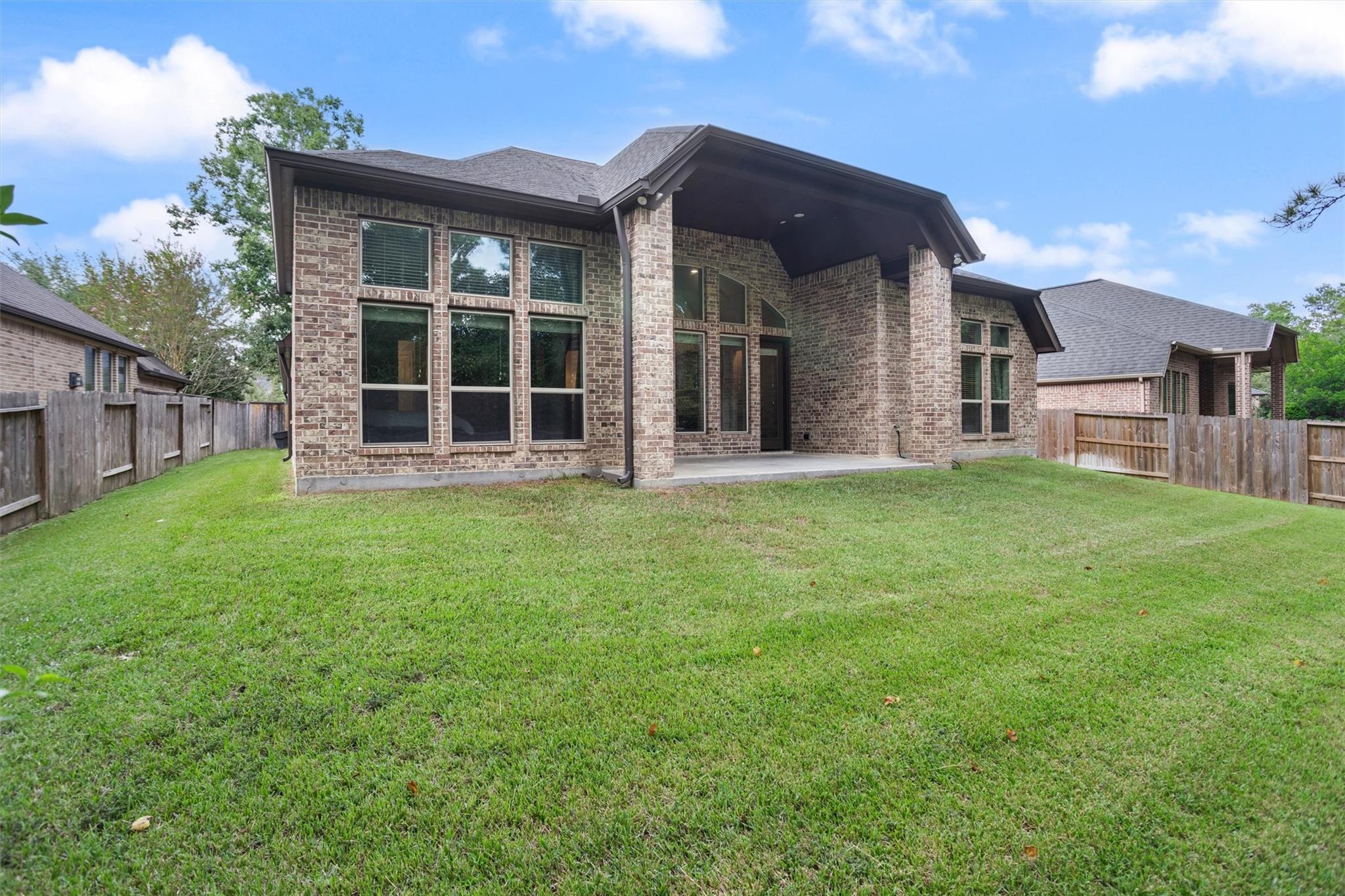 Brick home’s rear exterior with a covered patio and broad fenced lawn.