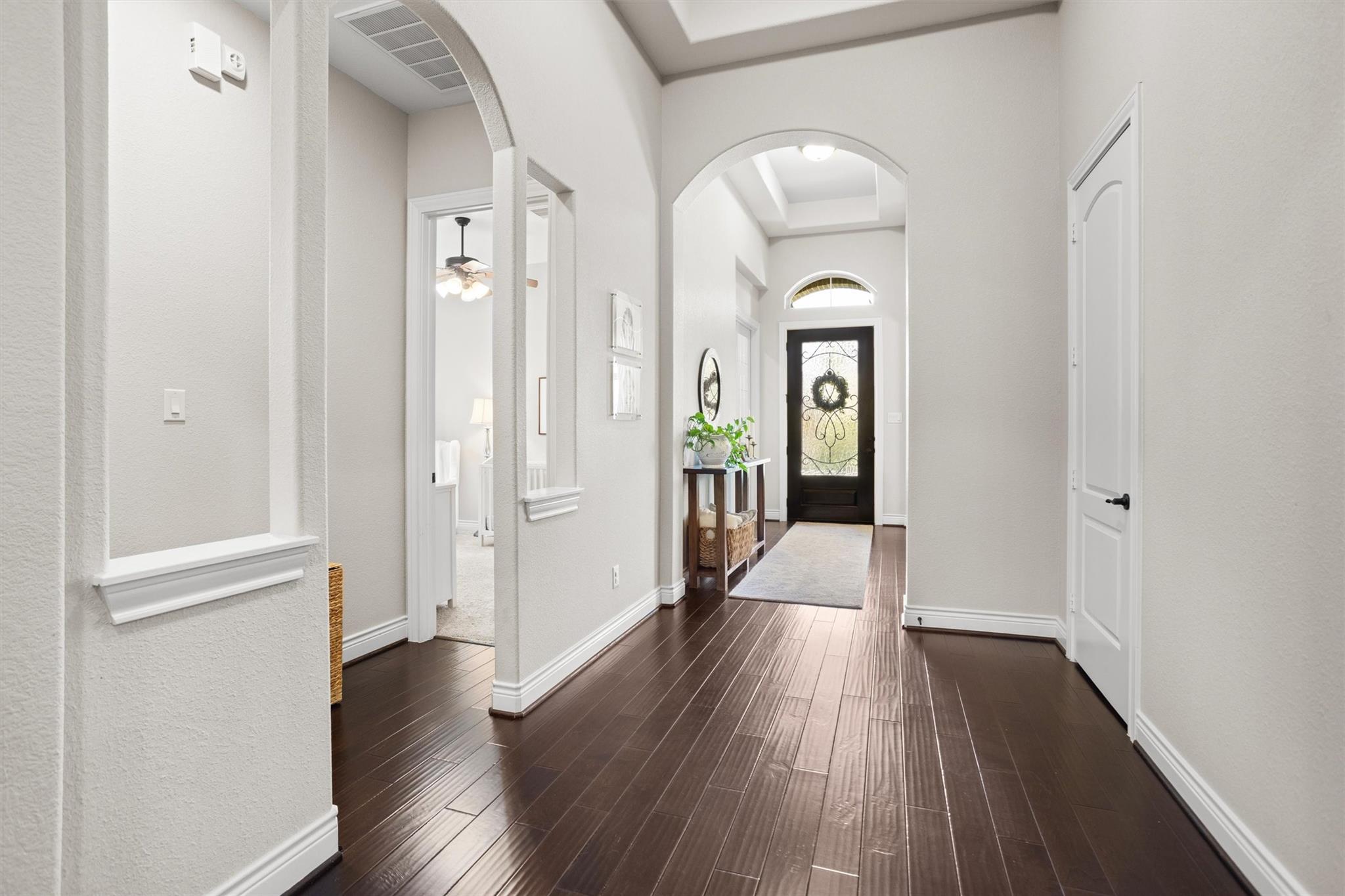 Entry hallway with dark wood floors, arched openings, and a black decorative-glass front door.