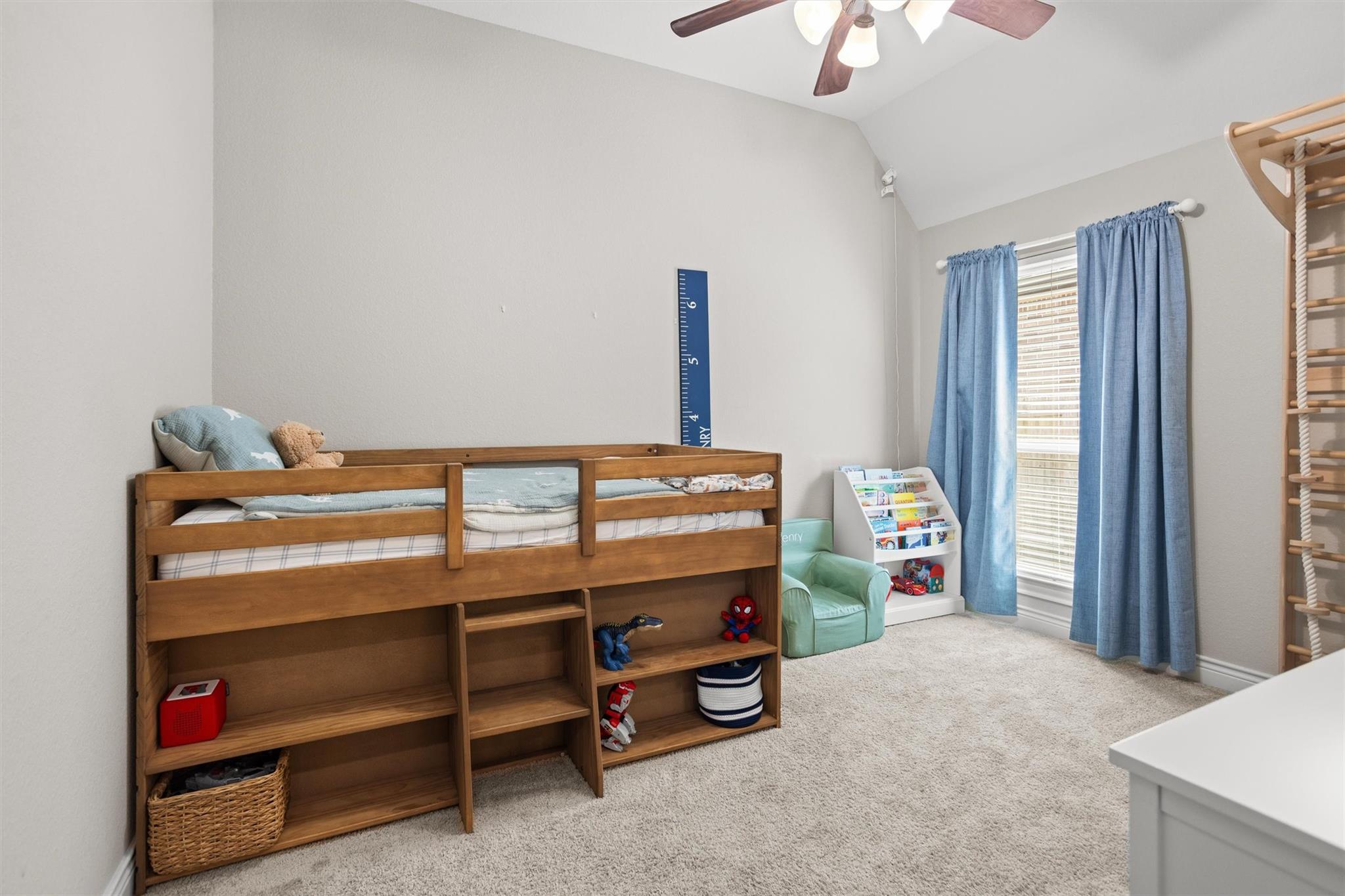 Children’s bedroom with a wooden loft bed, toy storage, blue curtains, and a reading nook.