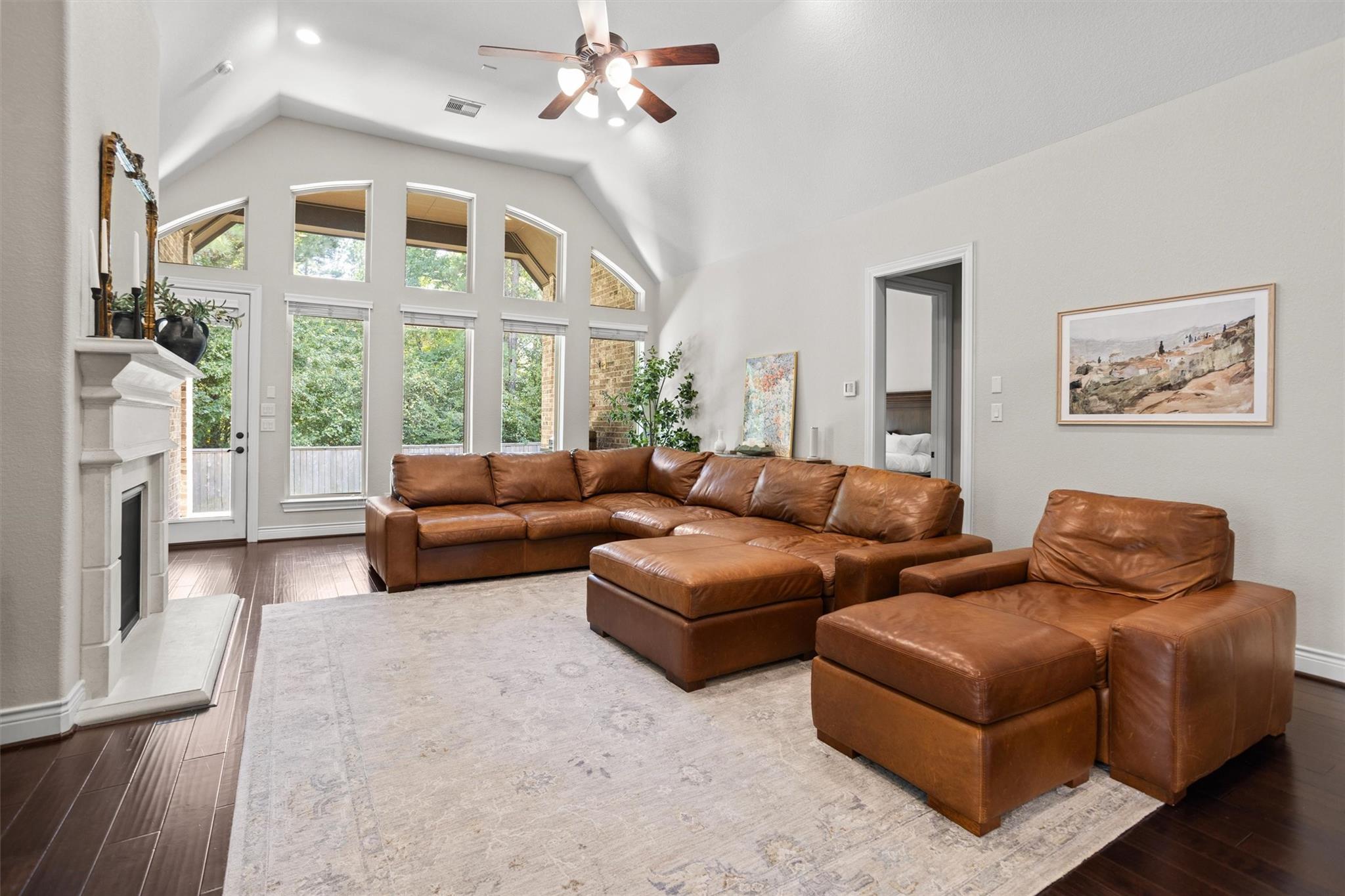 Living room with vaulted ceiling, tall windows, white fireplace, and brown leather seating.