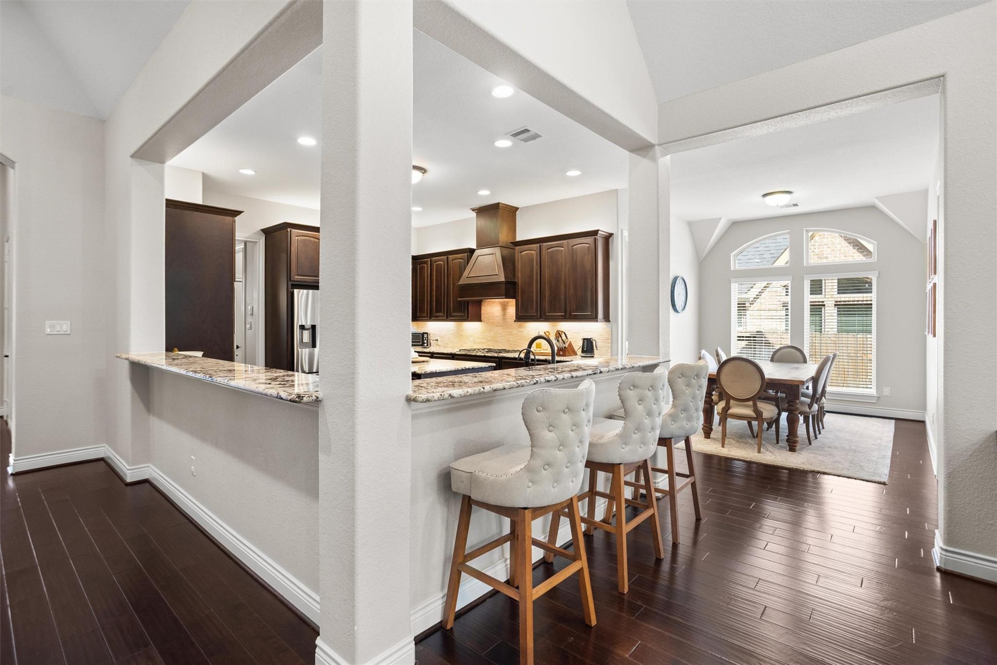 Open-plan kitchen and dining area with a granite breakfast bar, dark wood cabinets, and tall windows.