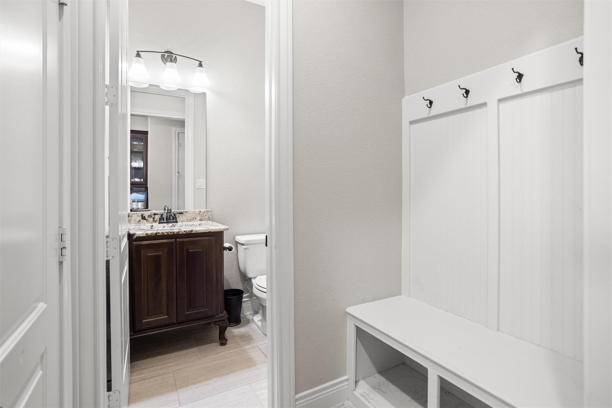 Bathroom with dark wood vanity beside a white built-in bench and wall hooks.