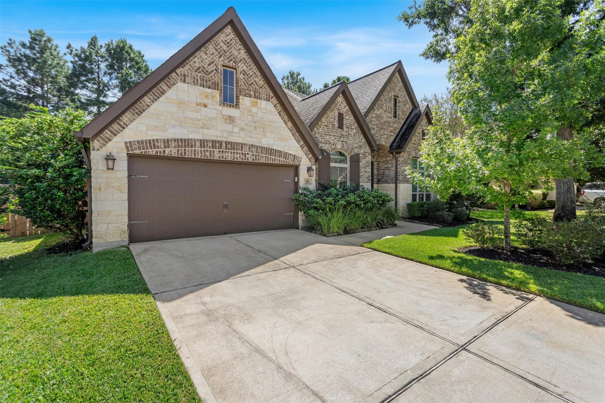 Stone-and-brick house with peaked gables, a brown two-car garage, and a wide driveway.