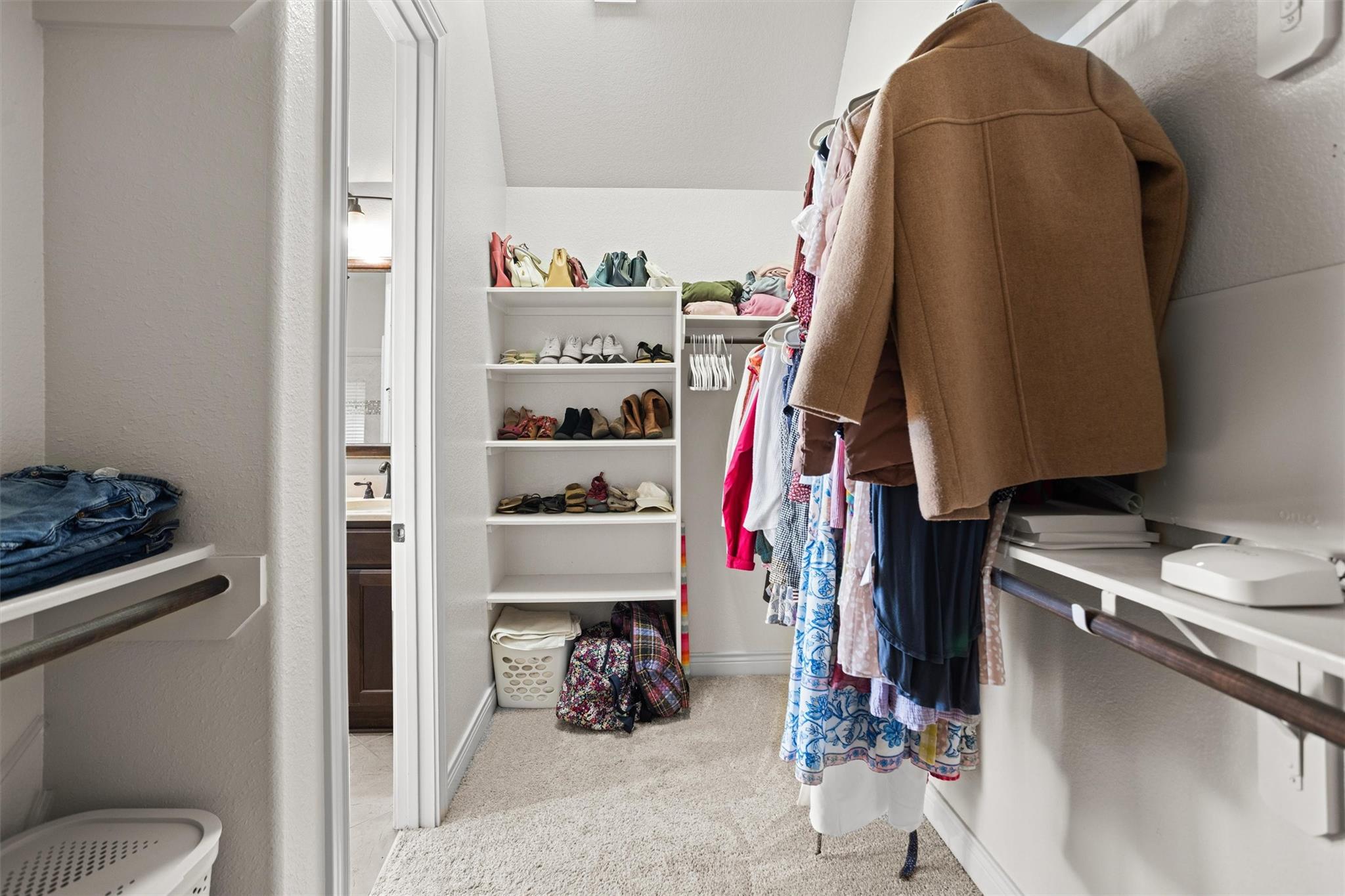Walk-in closet with built-in shoe shelves and hanging clothes, including a brown coat.
