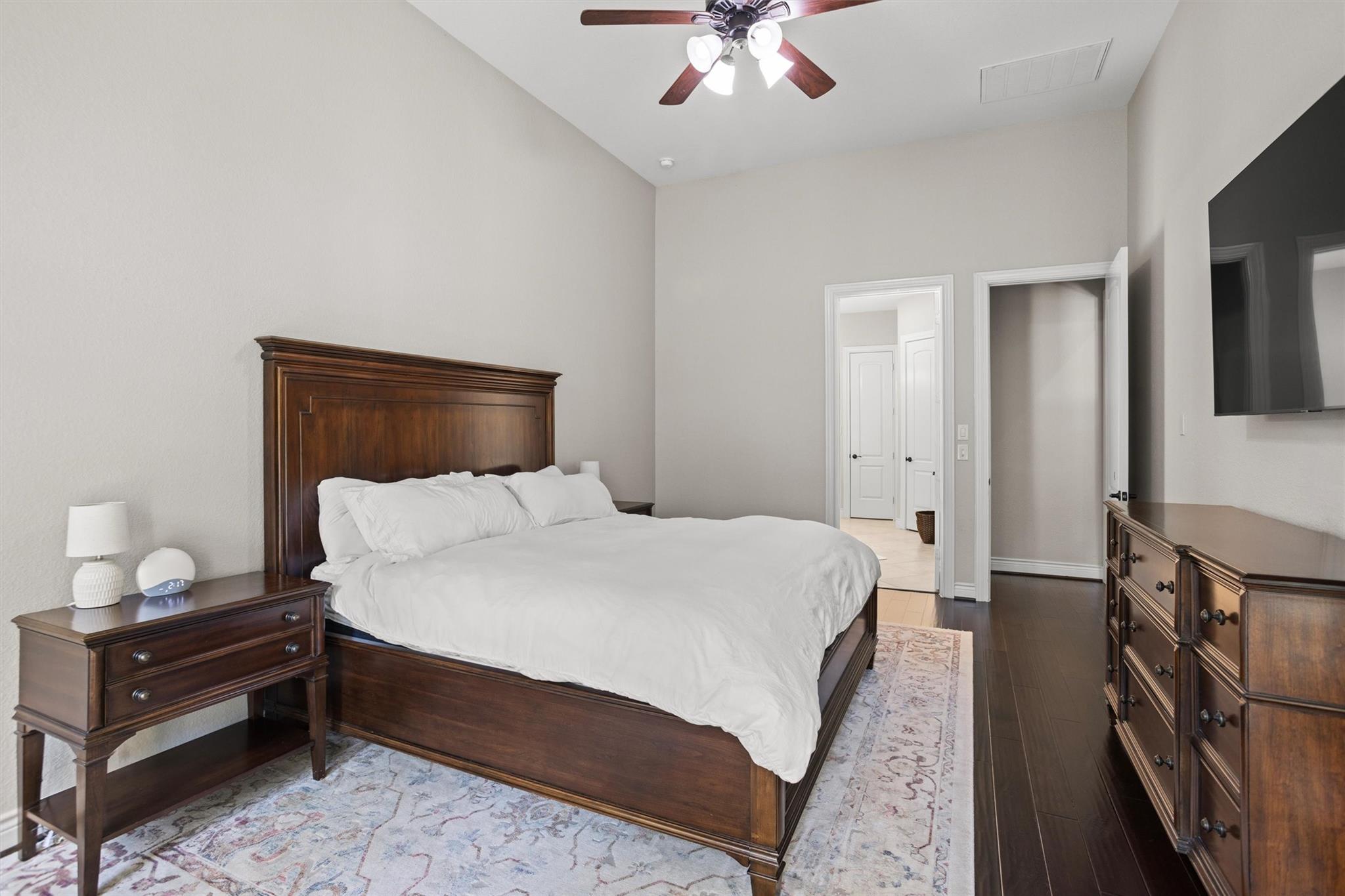 Bedroom with a dark wood bed, white bedding, matching dresser, and patterned rug.