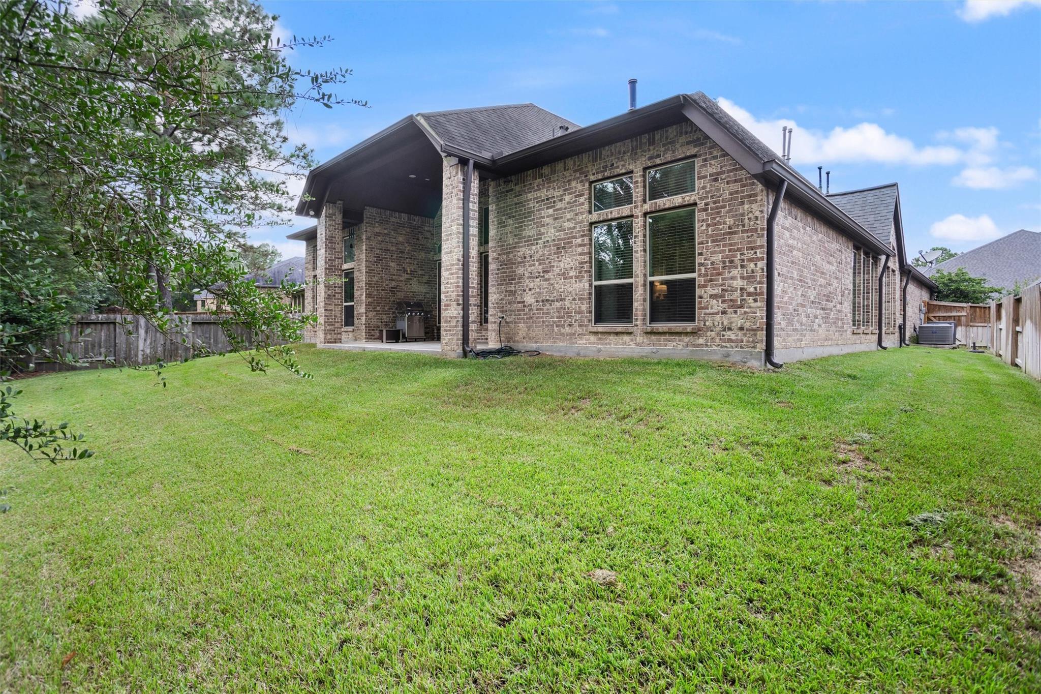 Brick house with a covered patio and grill overlooking a fenced grassy backyard.