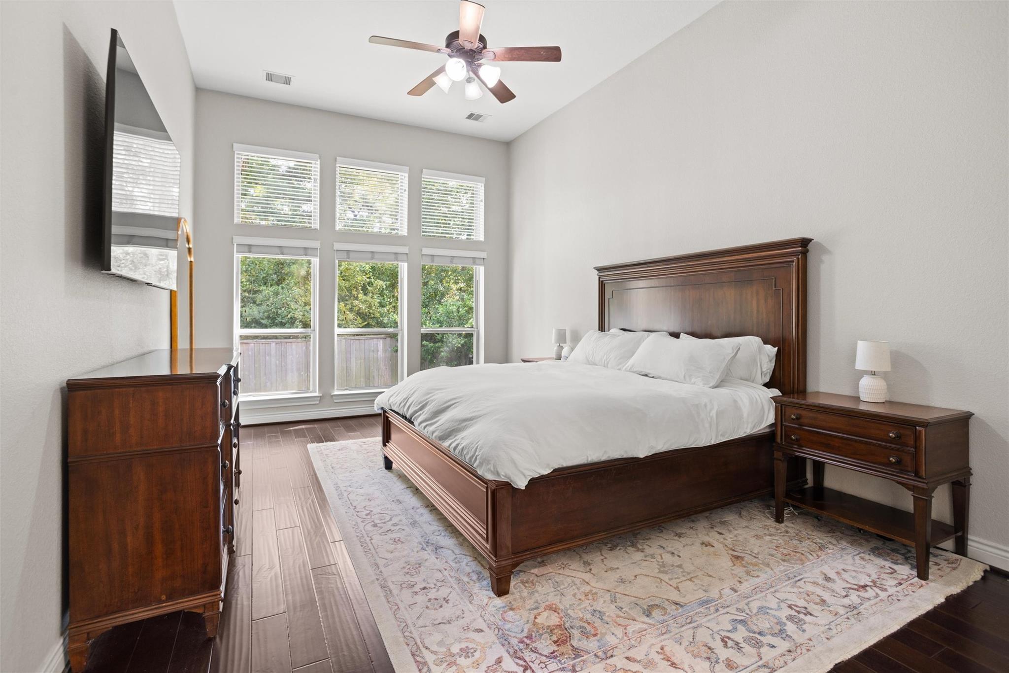 Furnished bedroom with a dark wood bed, white bedding, and tall windows overlooking trees.