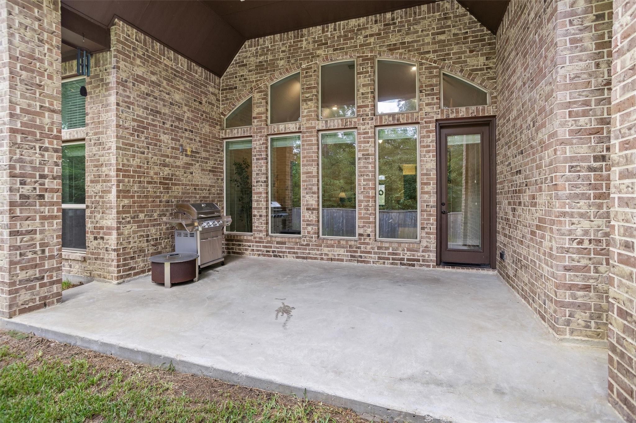Covered brick patio with a stainless steel grill, tall windows, and a glass door.