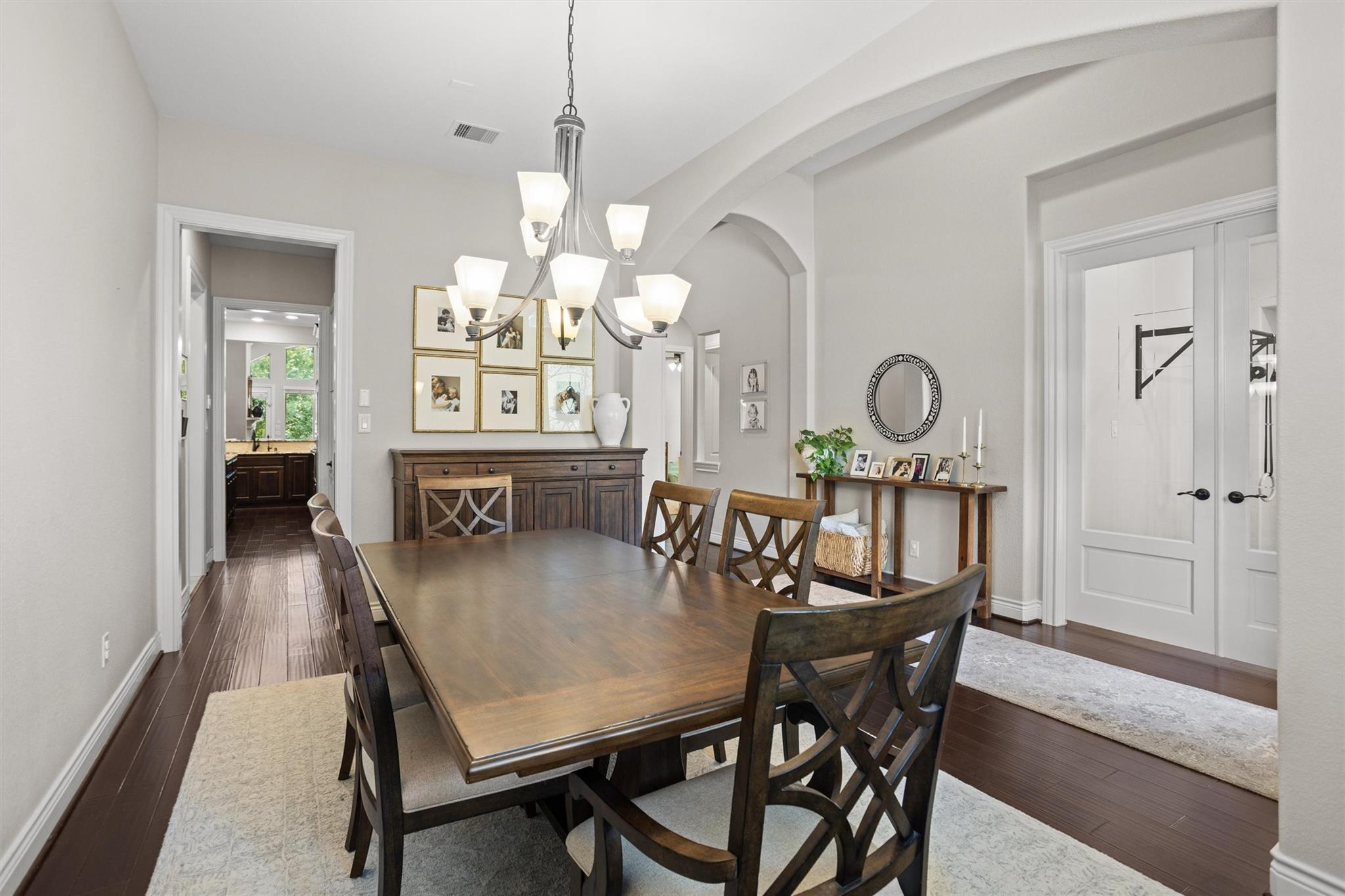 Dining room with a dark wood table, cross-back chairs, chandelier, and arched openings.