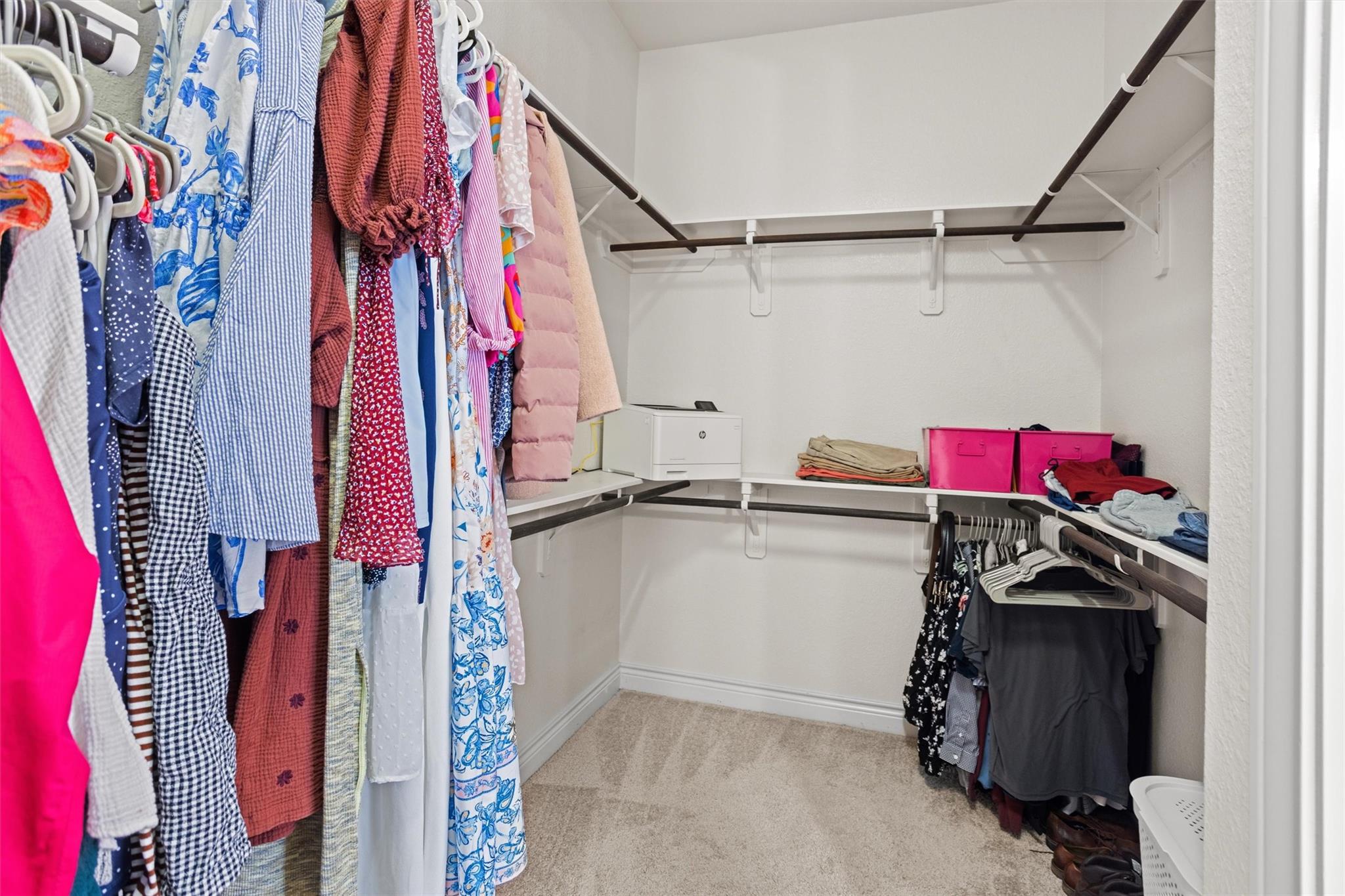 Walk-in closet with wraparound shelving, colorful hanging clothes, folded garments, and pink storage bins.