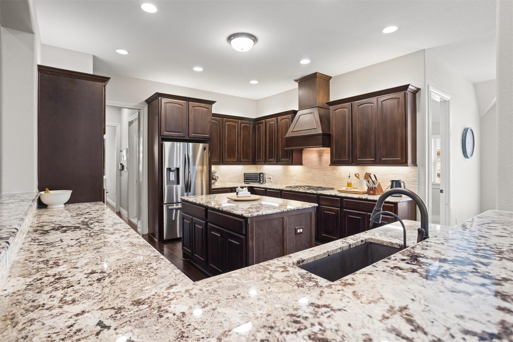 Kitchen with dark wood cabinetry, granite counters, a large island, and stainless steel appliances.