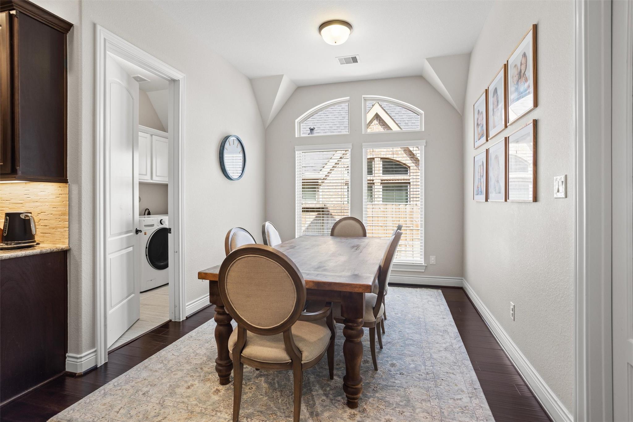 Dining room with a wood table beneath arched windows and a doorway to the laundry room.