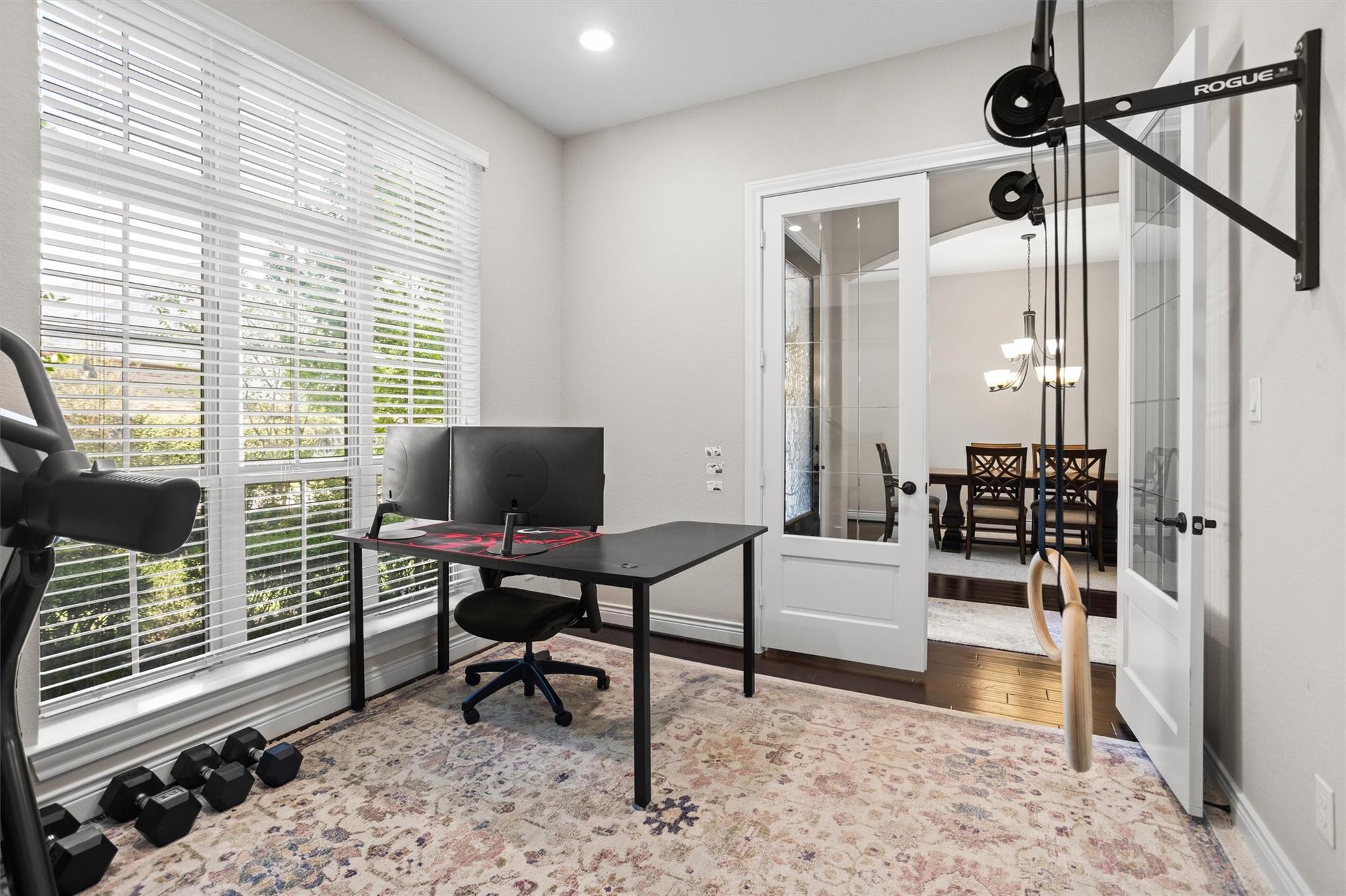 Home office and workout room with a black desk, dumbbells, and French doors opening to a dining room.