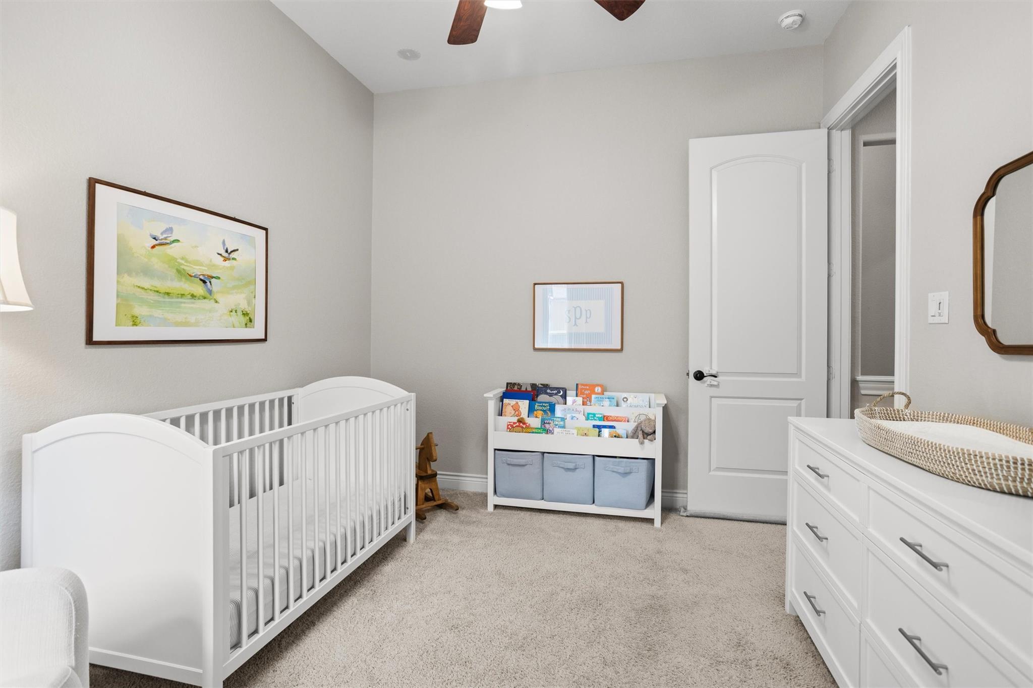 Nursery with a white crib, dresser and woven changing basket, and children’s books in a low bookcase.
